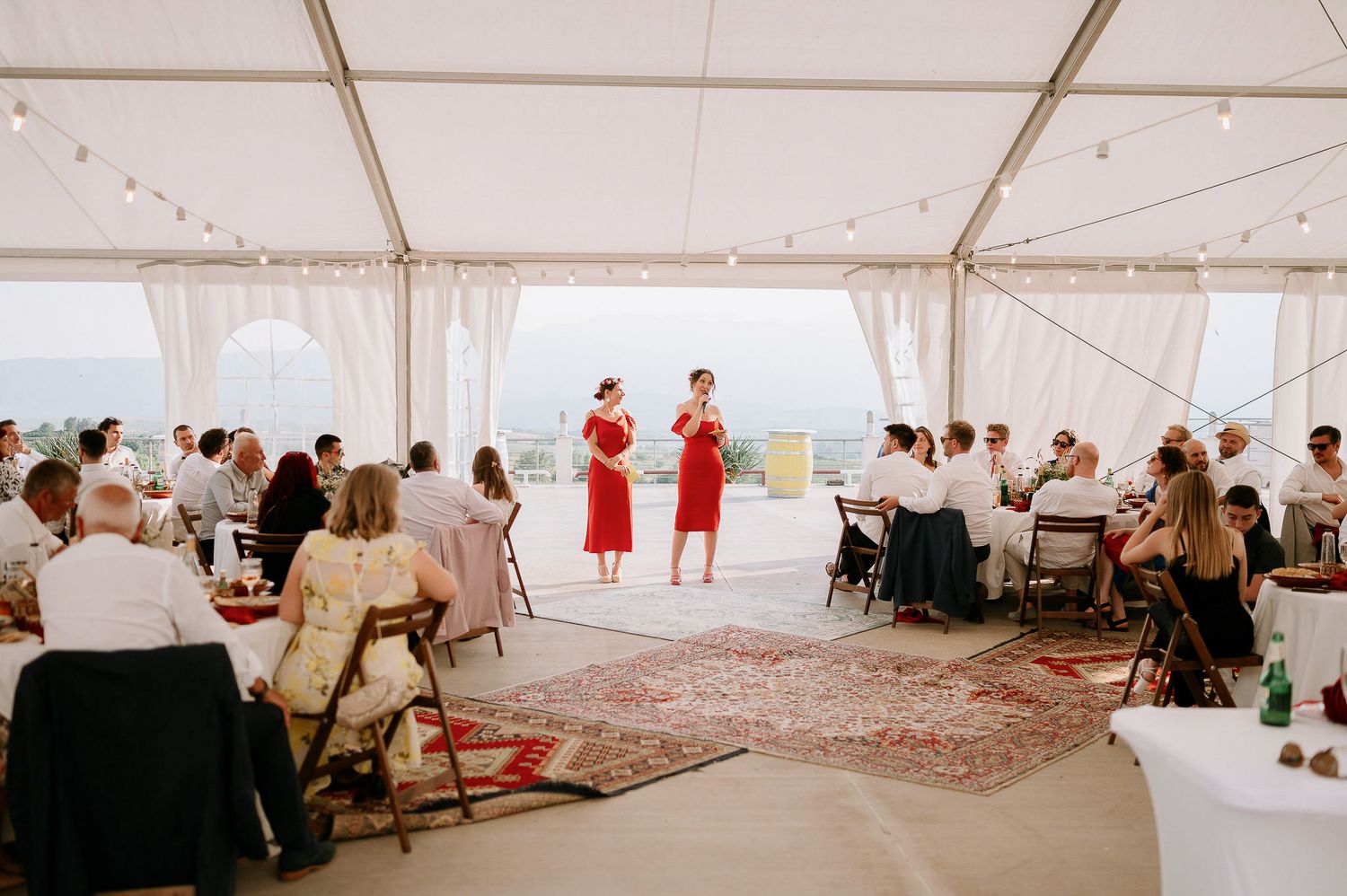 Wide view of a wedding reception tent with guests seated at multiple tables.