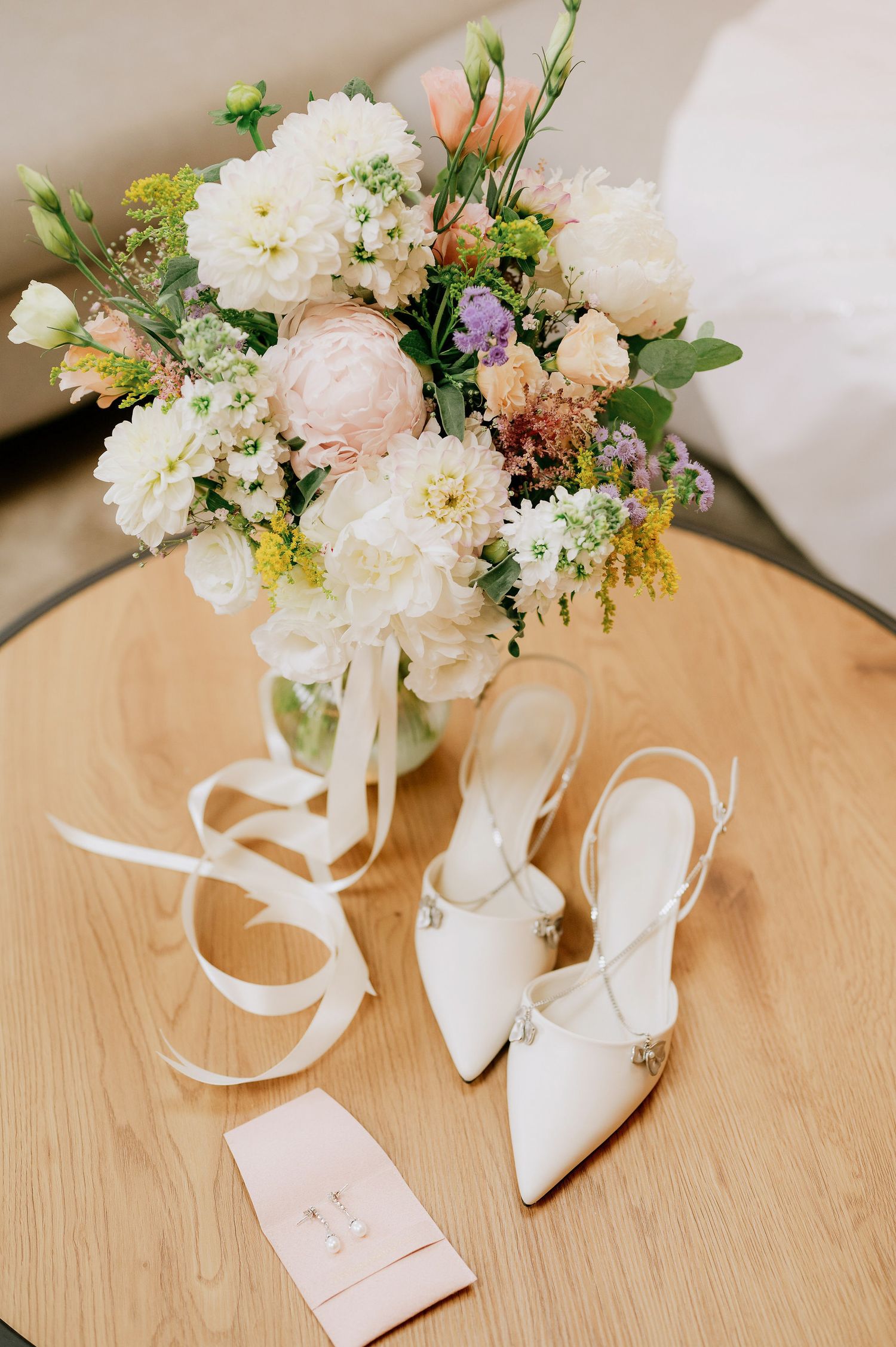White bridal shoes with floral bouquet on wooden surface.