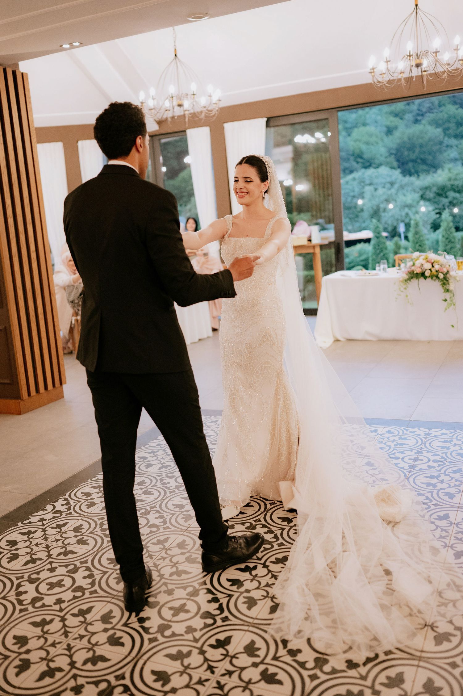 Couple dancing in an elegant reception venue with patterned floor and large windows.
