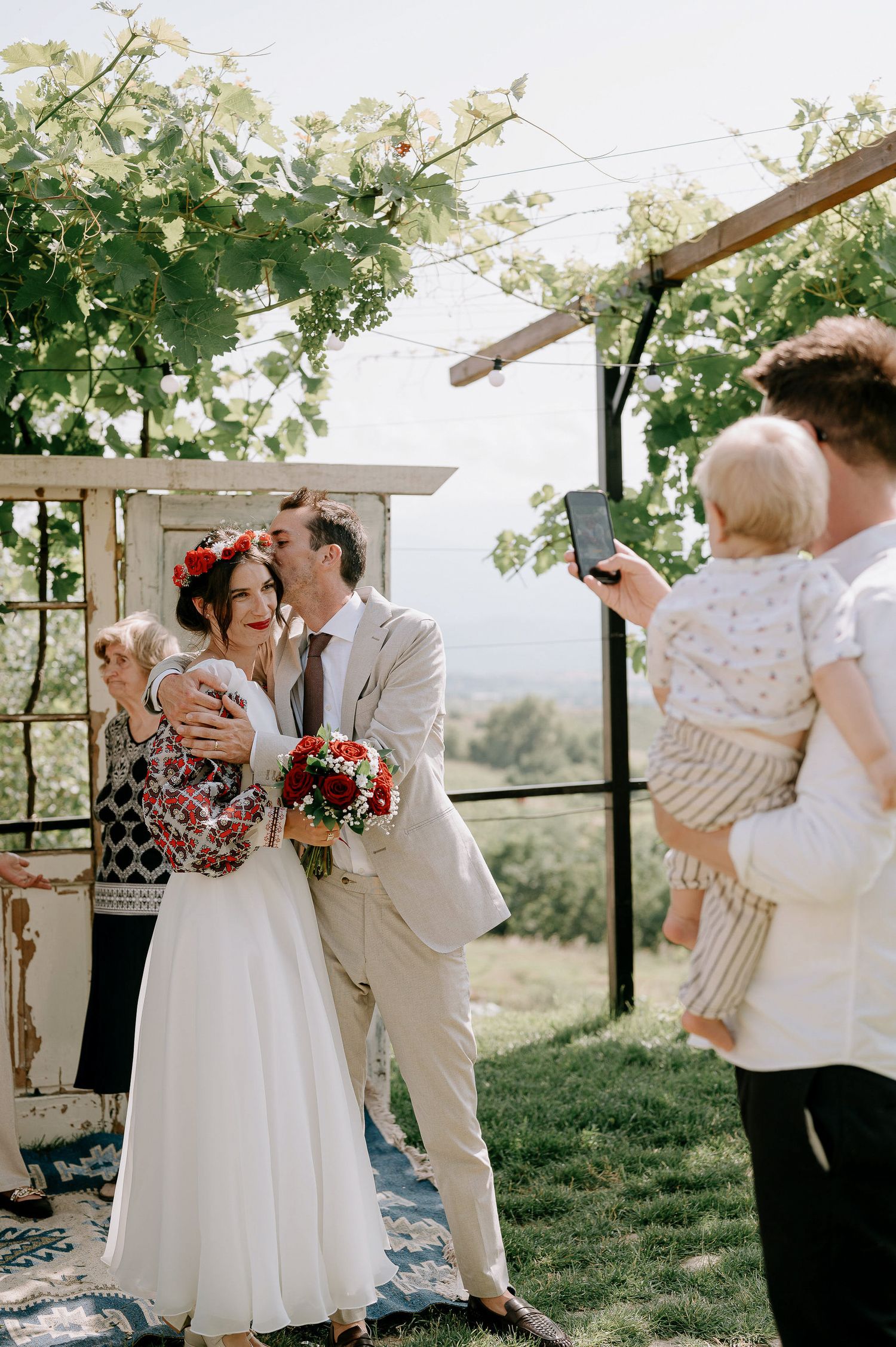 Outdoor wedding celebration with couple dancing under green trees and natural lighting.