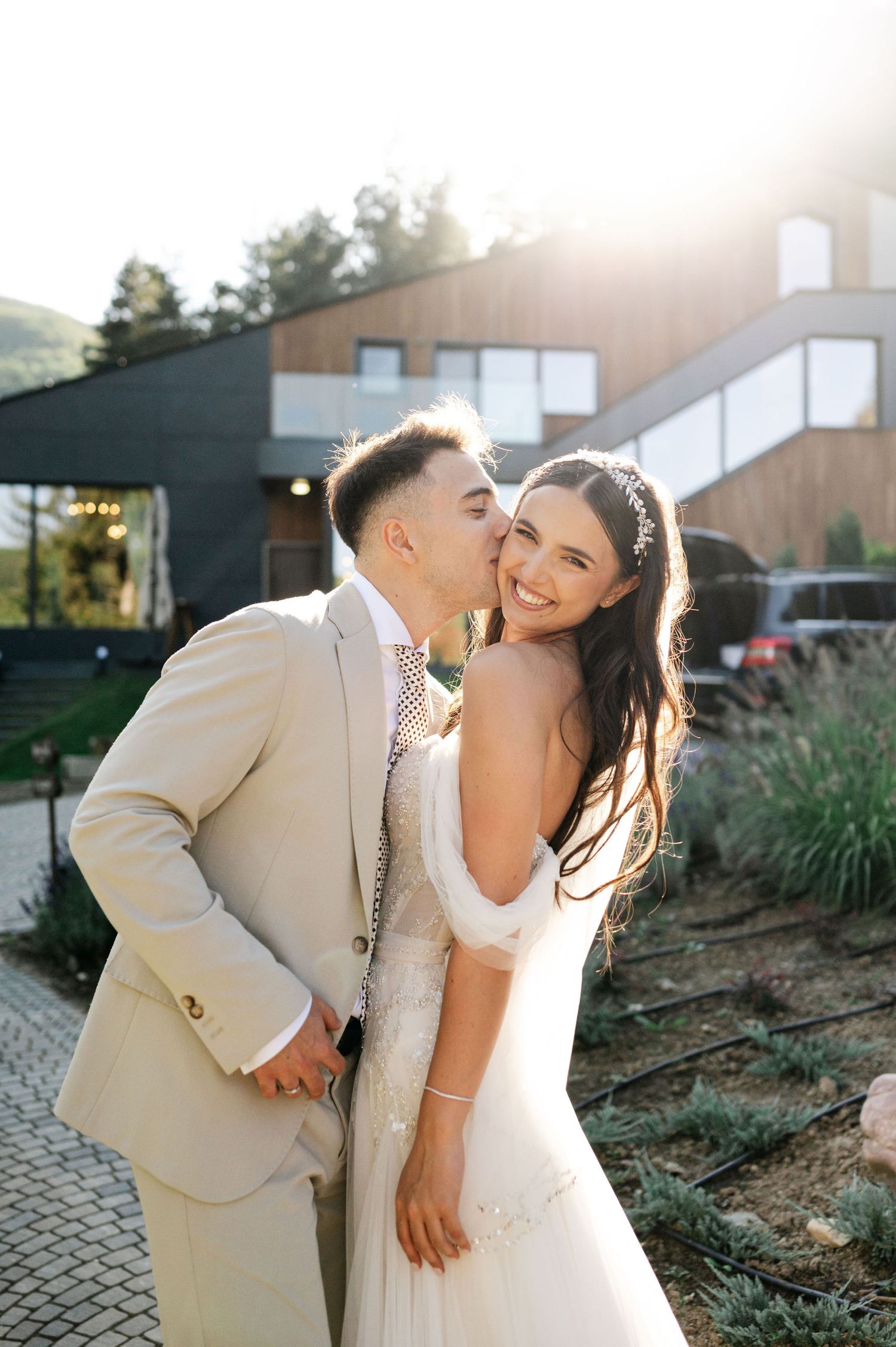 A joyful wedding couple embraces on a paved outdoor terrace during sunset.