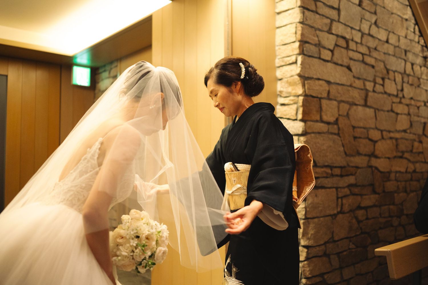 Elegant bridal fitting scene with traditional white wedding dress being styled in warm-lit room.