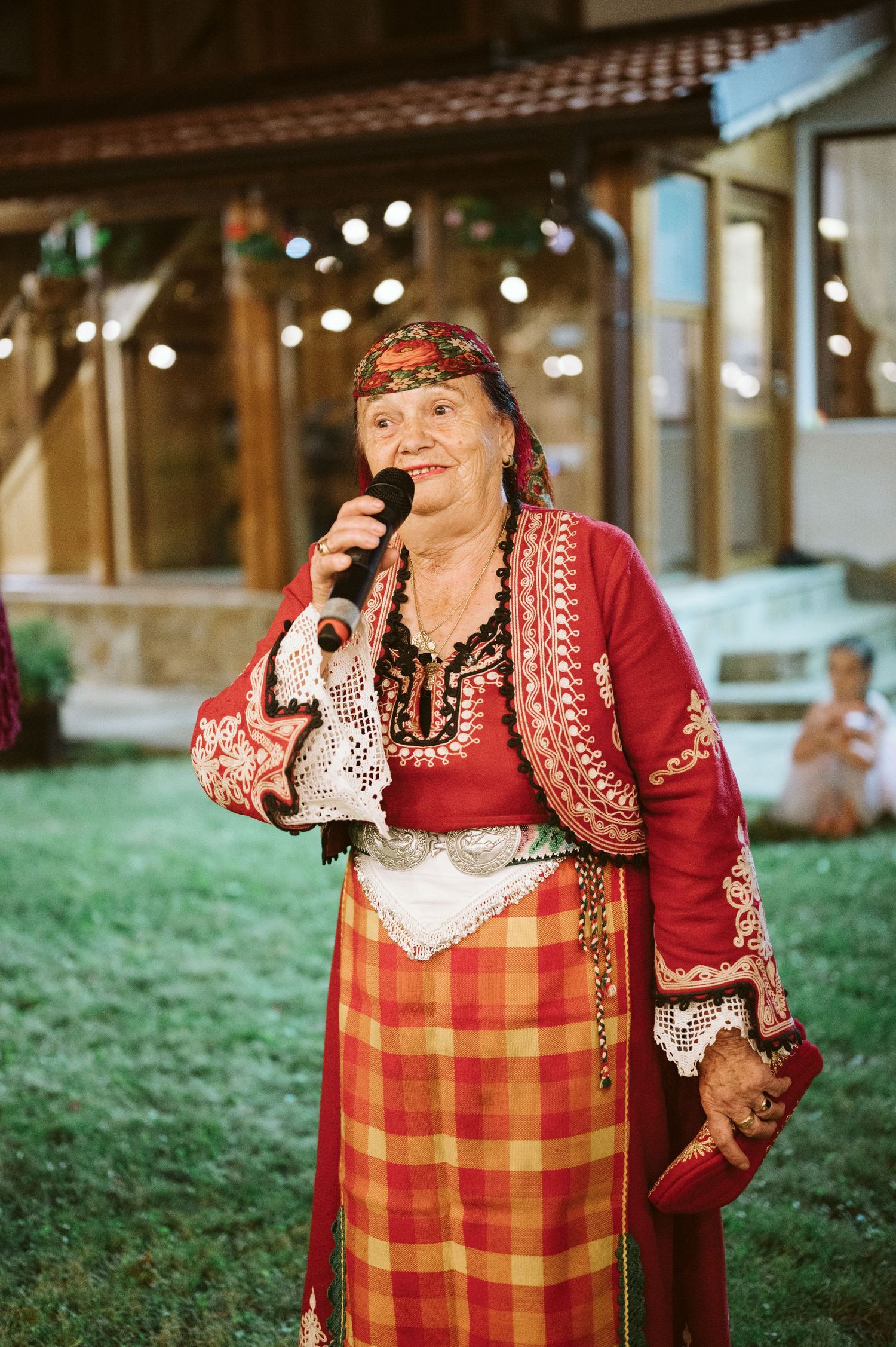Traditional folk performer in red jacket and plaid apron performing at outdoor venue.