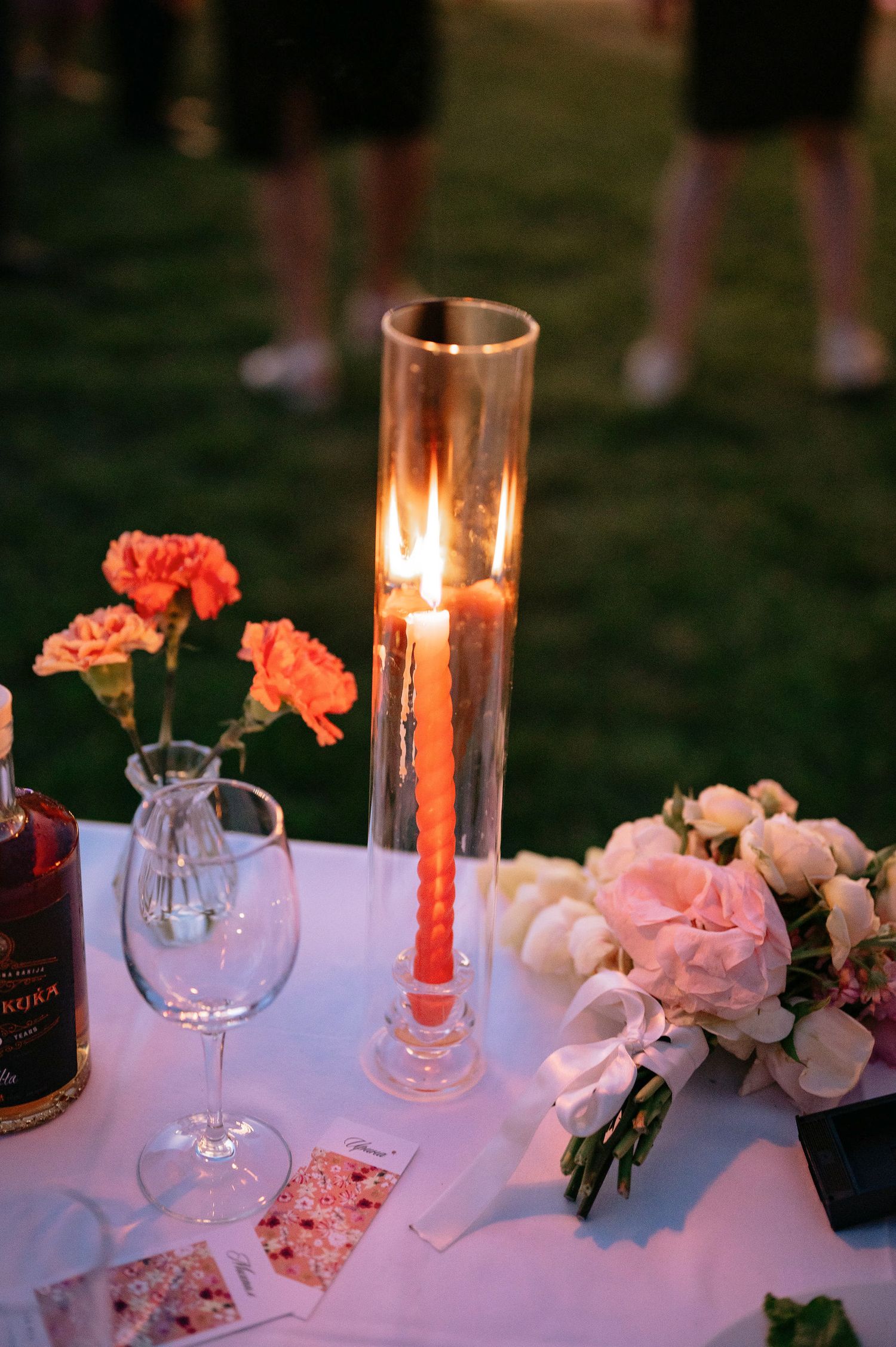 Elegant table settings with pink flowers and glowing candles create a romantic outdoor wedding reception atmosphere.