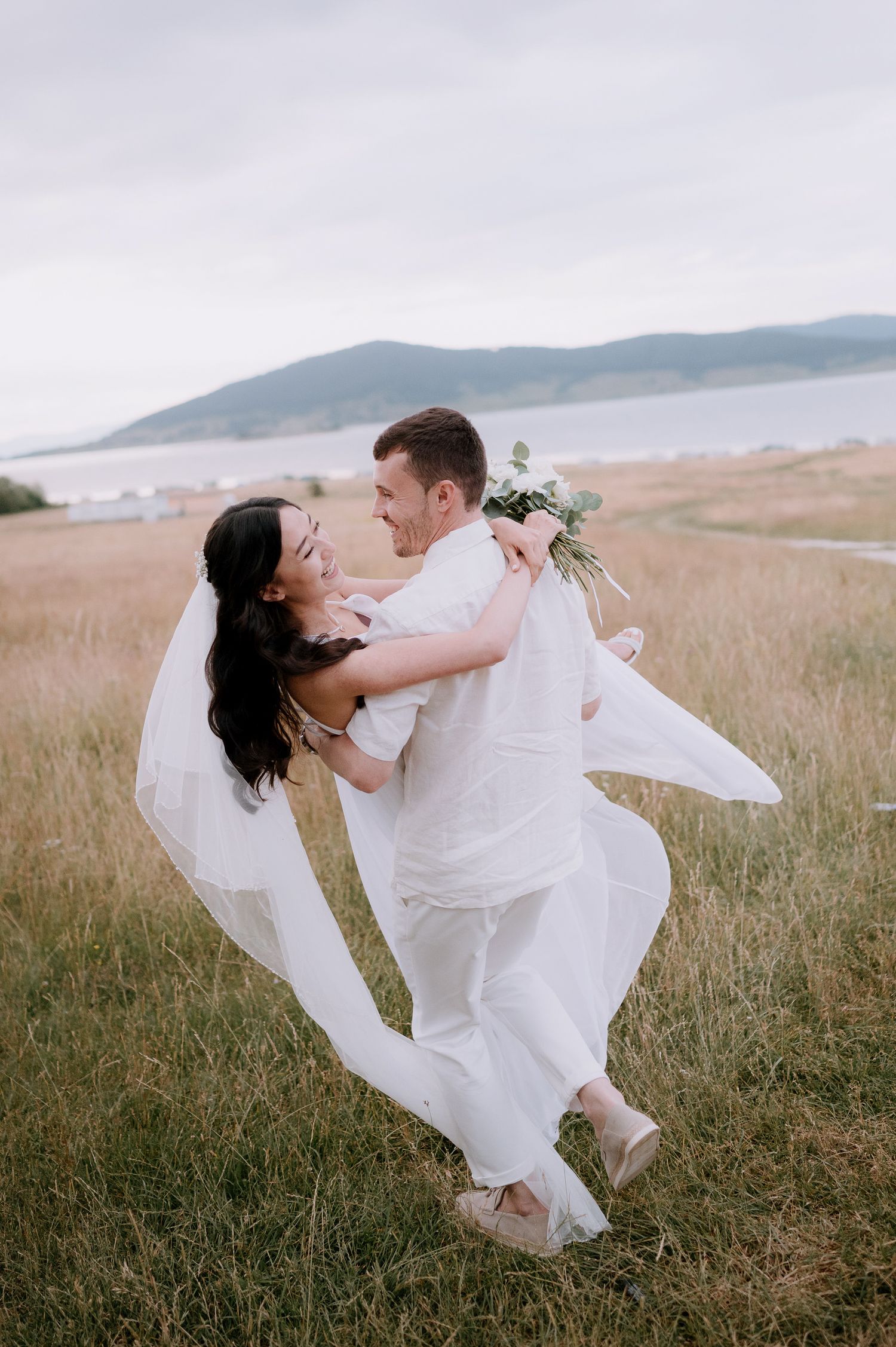 Wedding couple performs a dramatic dance lift against a scenic coastal landscape.