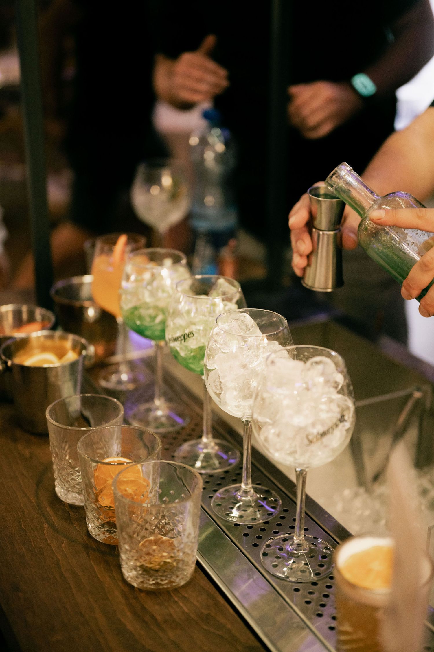 A sequence of cocktail preparation shots showing bartenders pouring drinks into crystal glasses filled with crushed ice.
