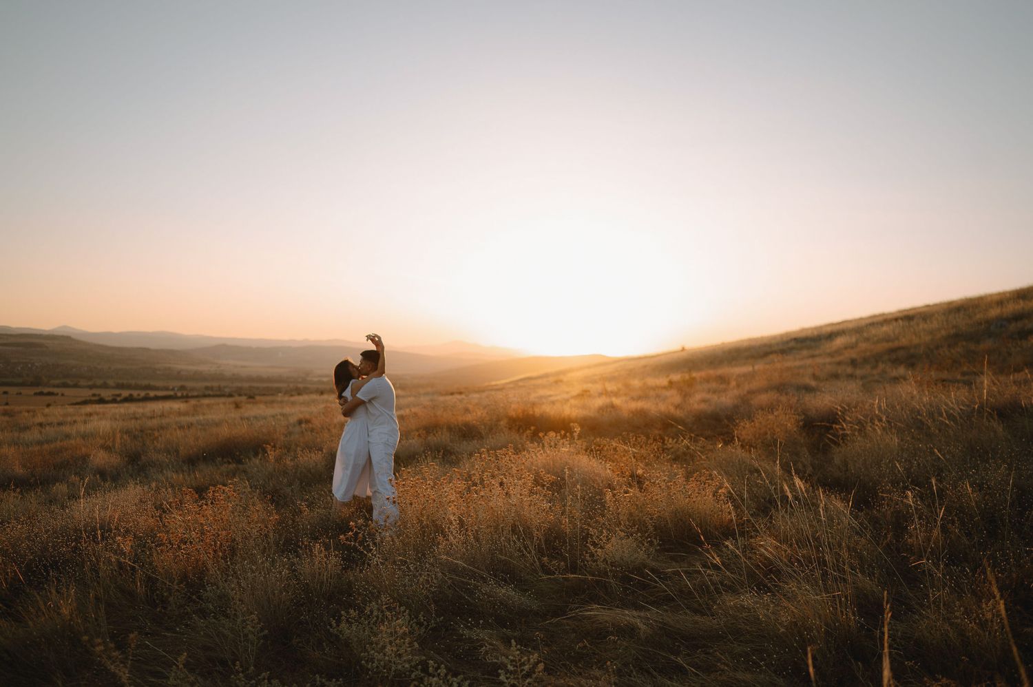 Dreamy landscape scene of figures in flowing white dress exploring rolling hills during golden hour.