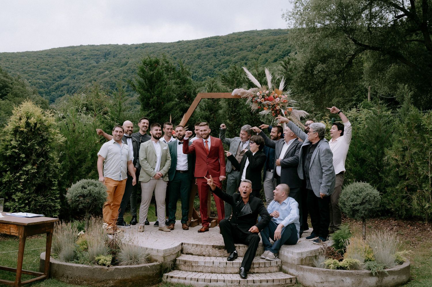 A celebratory group poses together on outdoor steps with mountain scenery in the background.