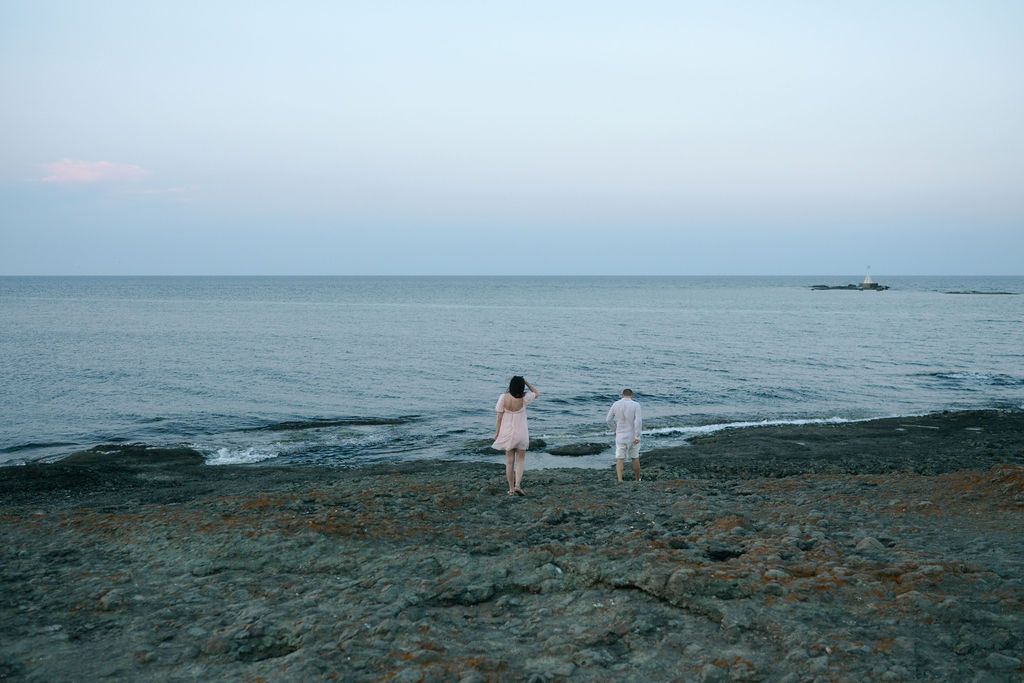 Serene coastal landscape with two distant figures exploring a rocky beach against a misty ocean backdrop.