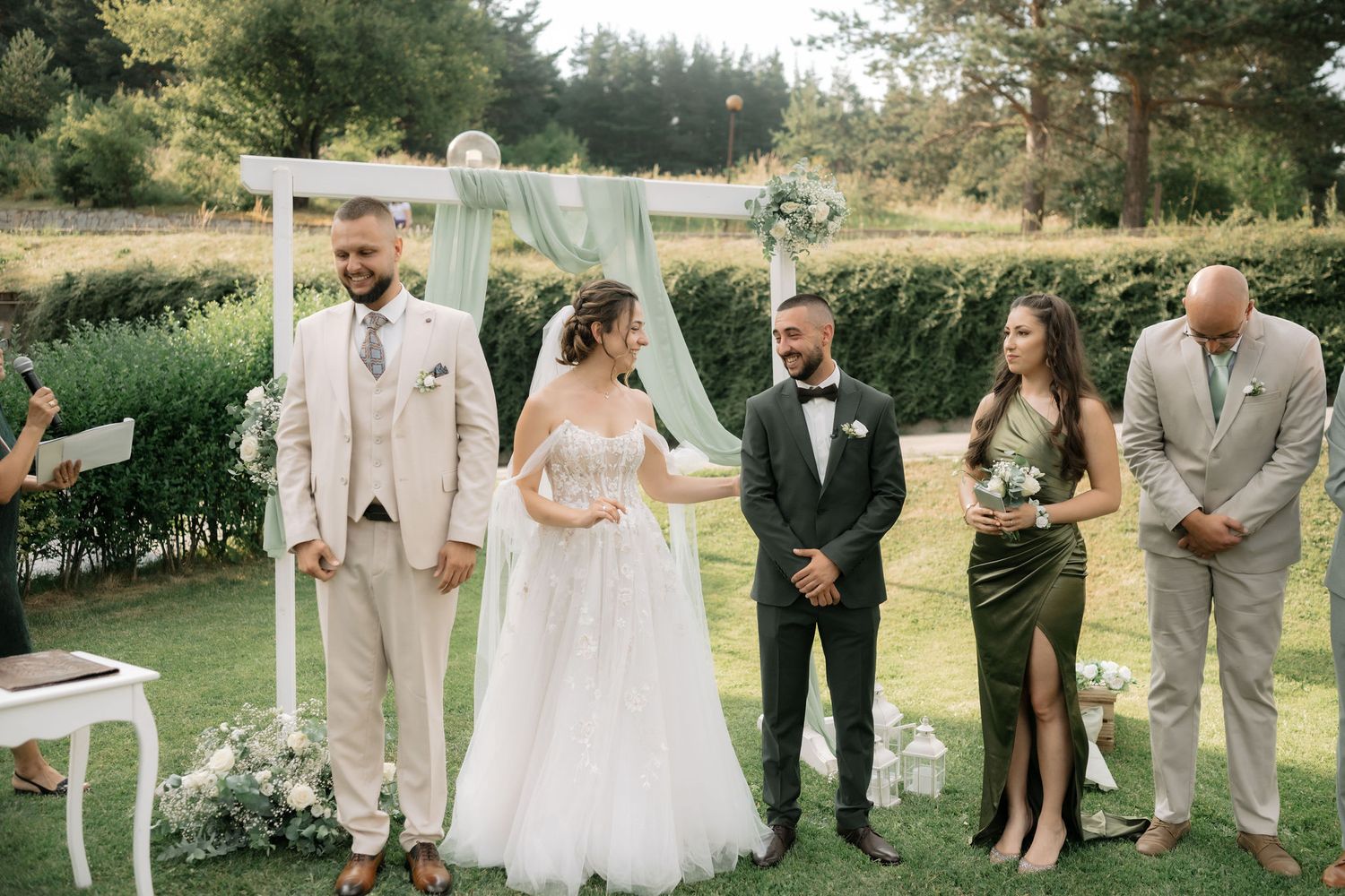 Wedding party in neutral beige and tan attire poses together on a sunny lawn during outdoor summer celebration.
