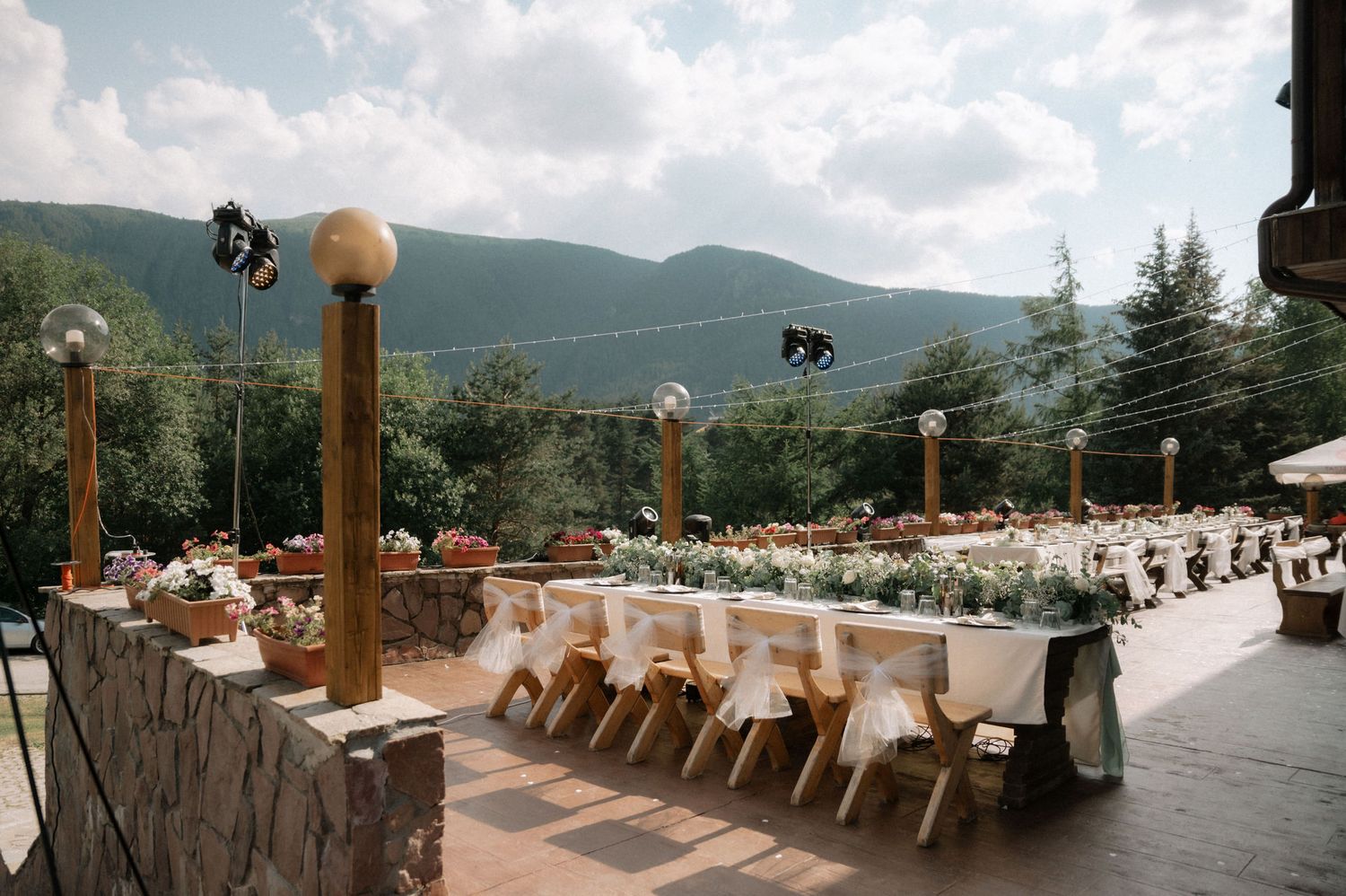 Panoramic mountain view from rustic wooden deck with chairs overlooking scenic valley landscape at sunset.