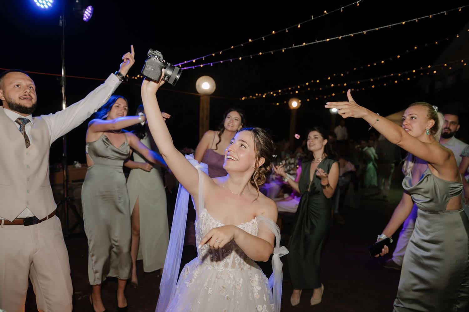 Wedding guests dancing and celebrating together on a dimly lit dance floor with blue lighting effects.