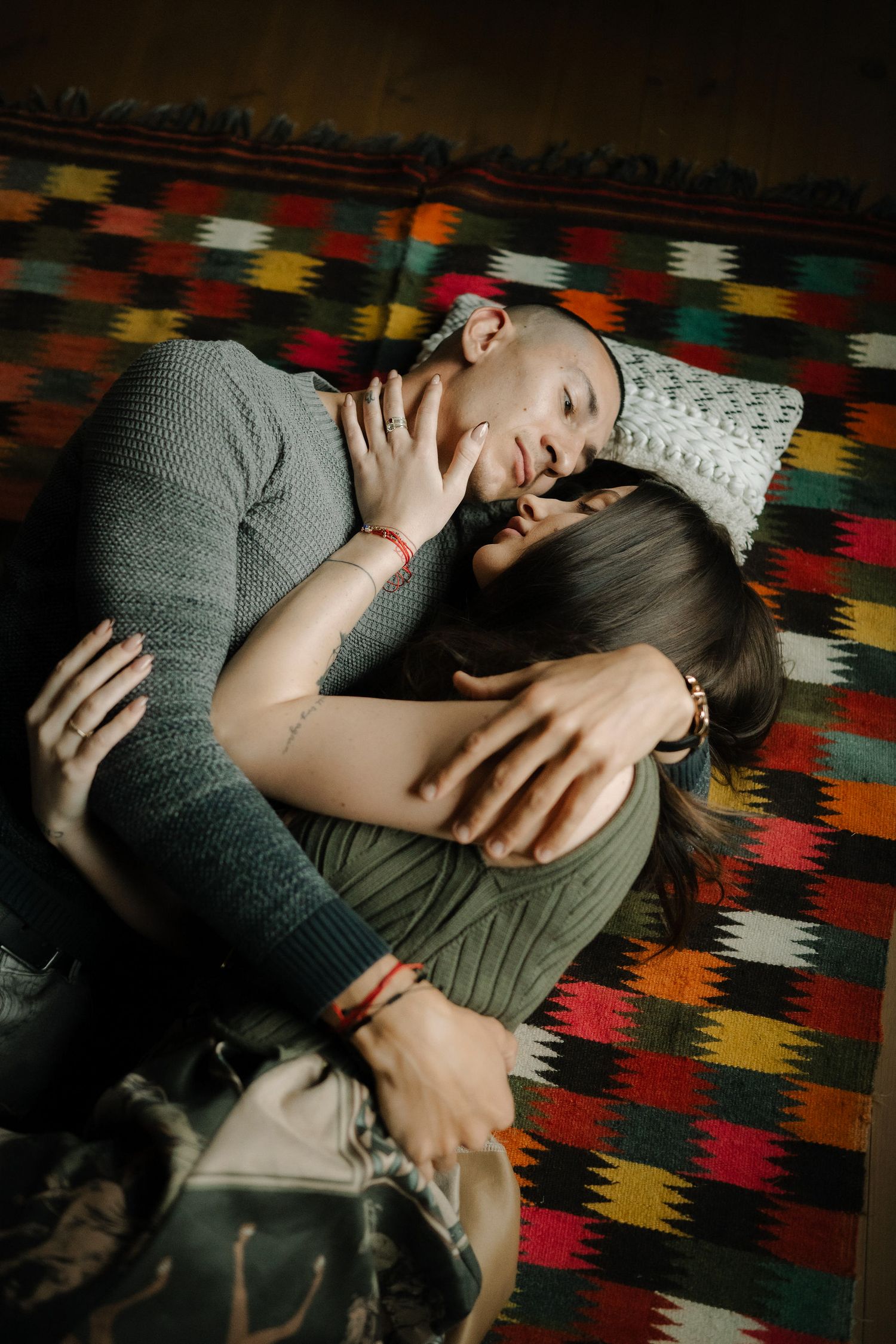 A person lies on a colorful patterned rug while wearing a gray sweater in moody lighting.