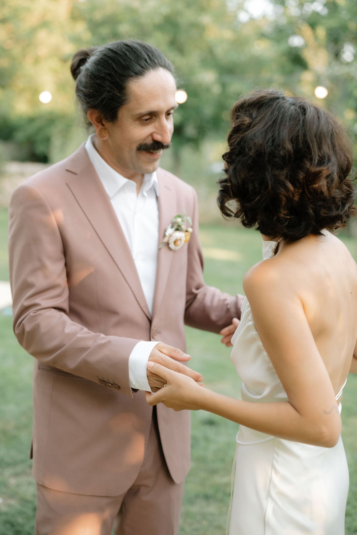 A couple in wedding attire share a romantic first dance moment outdoors in a garden setting.