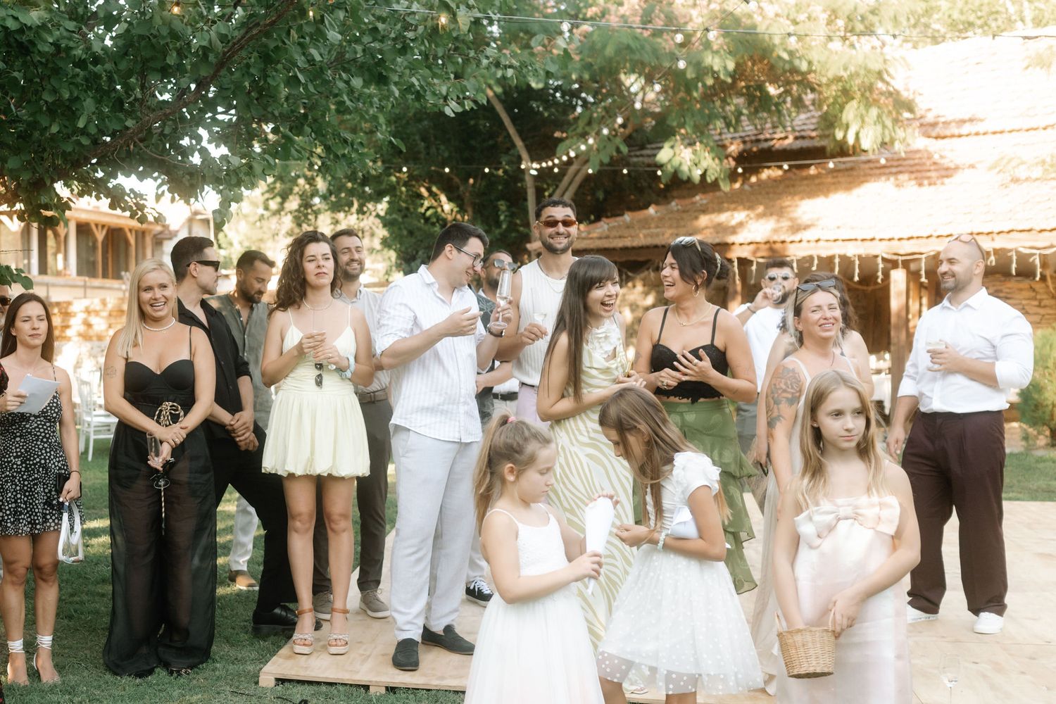 Wedding guests and bridal party gather for a celebratory toast in an outdoor garden setting.