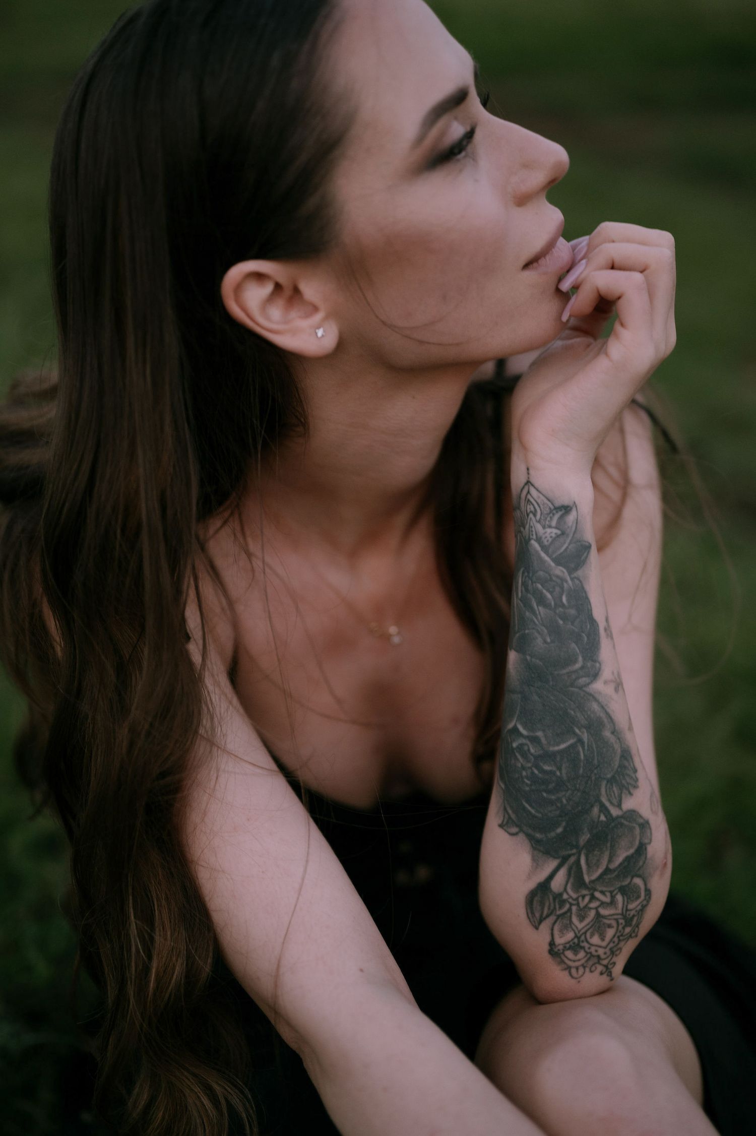 A person with long dark hair and a sleeve tattoo poses against a dark background in a series of artistic photos.
