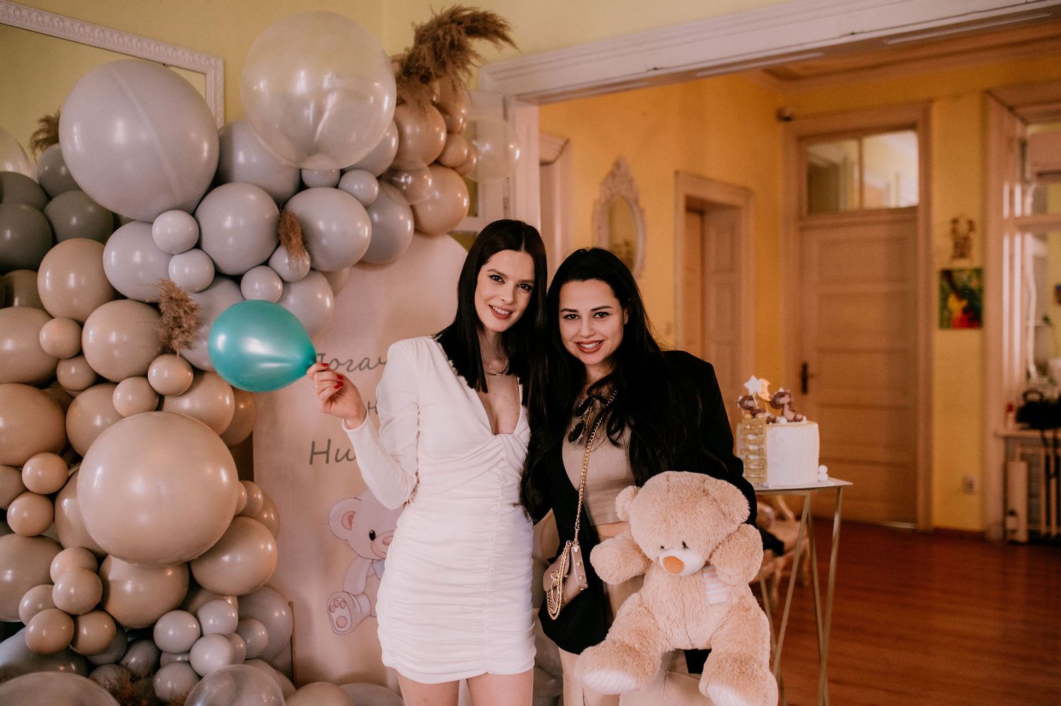 White and turquoise balloon decorations adorn an elegant indoor event space with warm lighting and wooden floors.