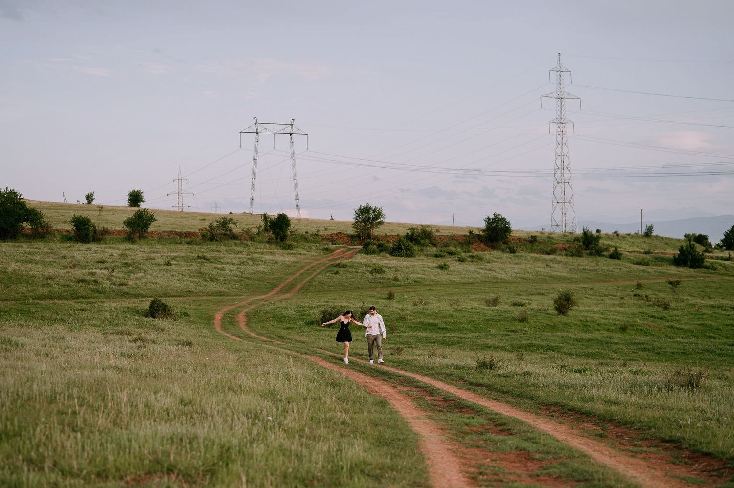 A winding dirt road curves through a rural grassland landscape with power lines visible in the distance.