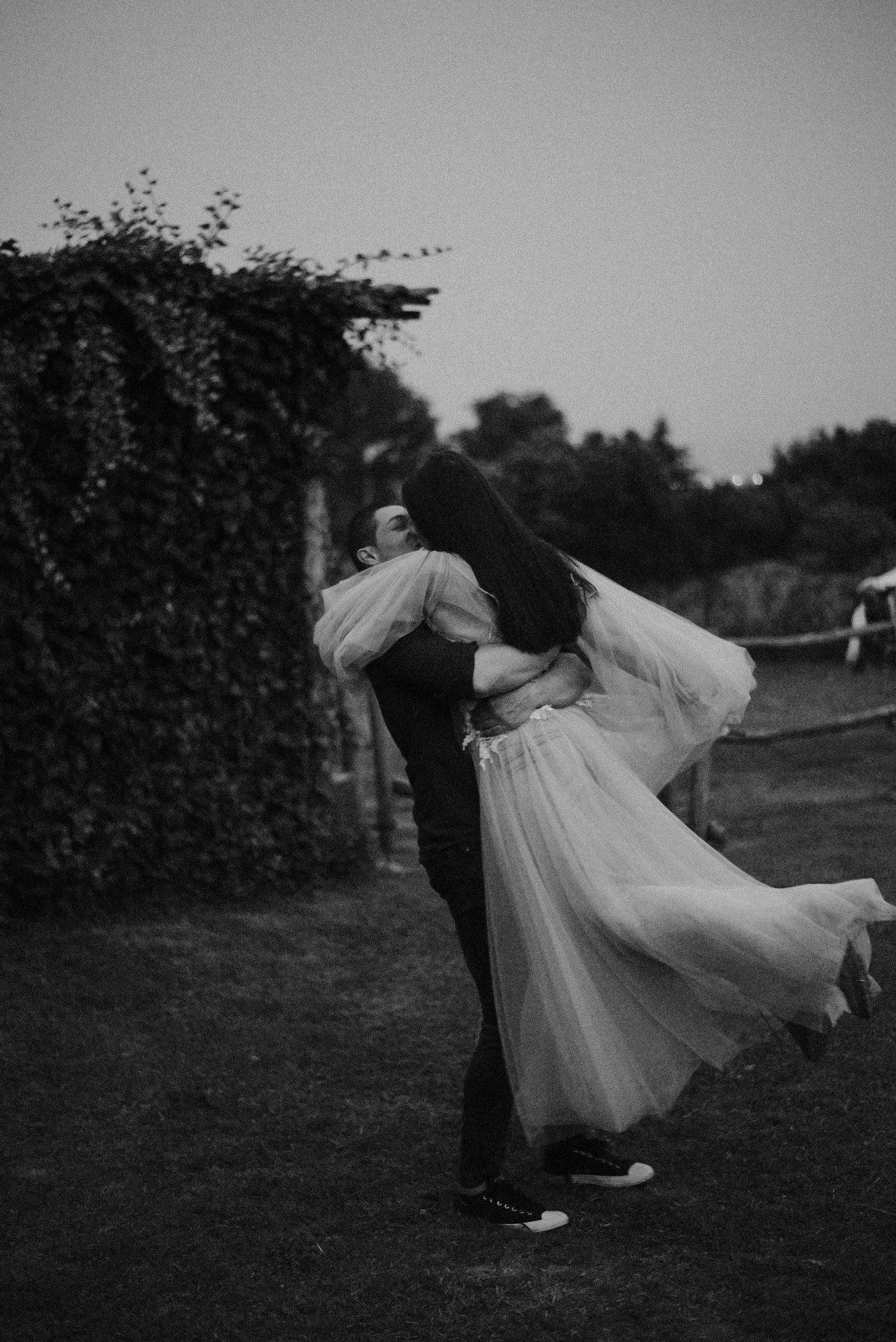 A couple dances together in a garden, with the person in a flowing white dress being dipped gracefully in black and white.