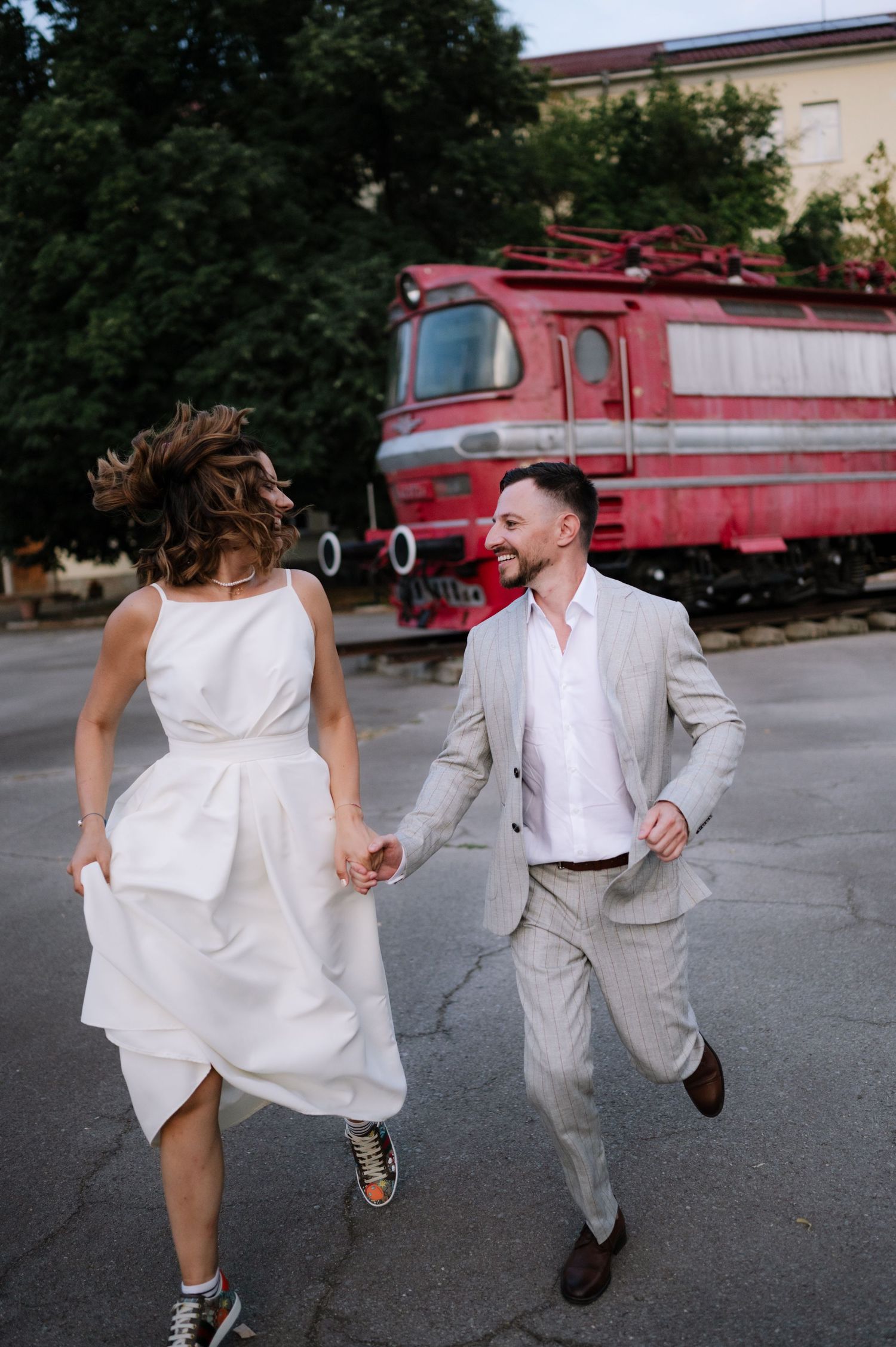 A couple dances and spins joyfully in front of a vintage red fire truck on a sunny day.
