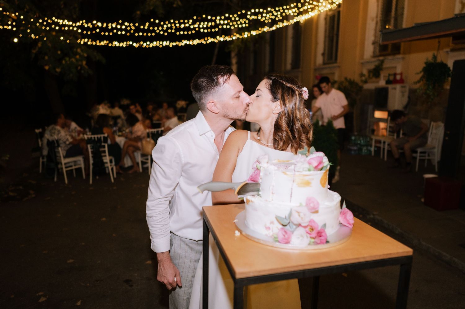 String lights illuminate a dance floor as couples enjoy a romantic evening celebration at an indoor venue.