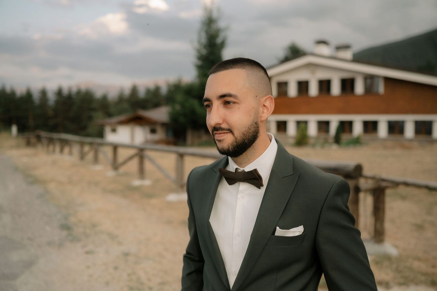 Wedding party poses in formal attire against scenic mountain backdrop with cloudy skies.