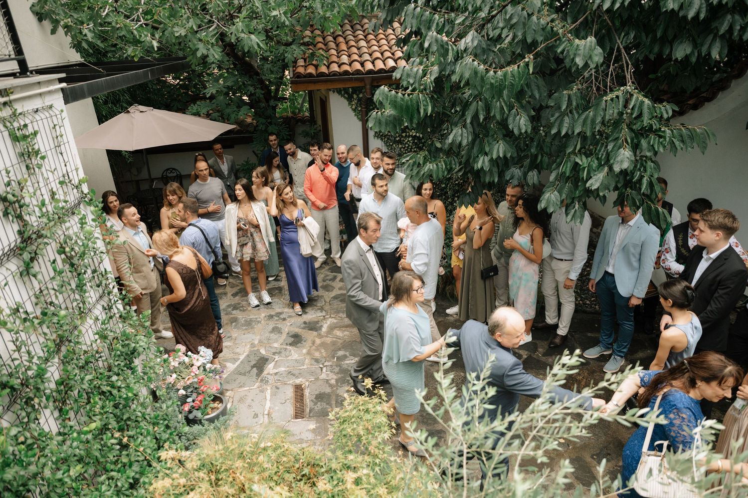 Wedding guests gathered outdoors under lush green trees for a garden celebration.