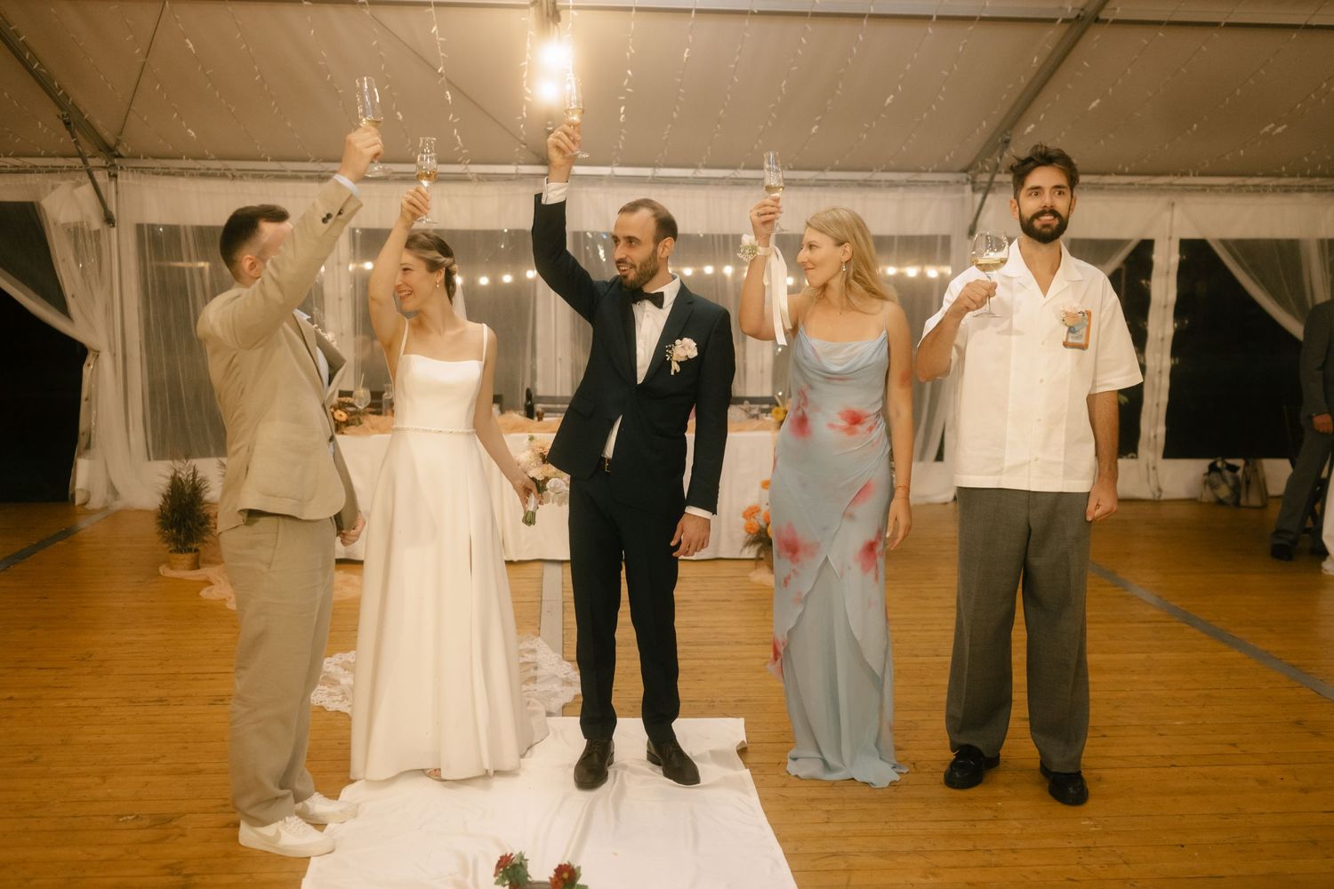Wedding party dancing together on wooden dance floor during reception celebration.