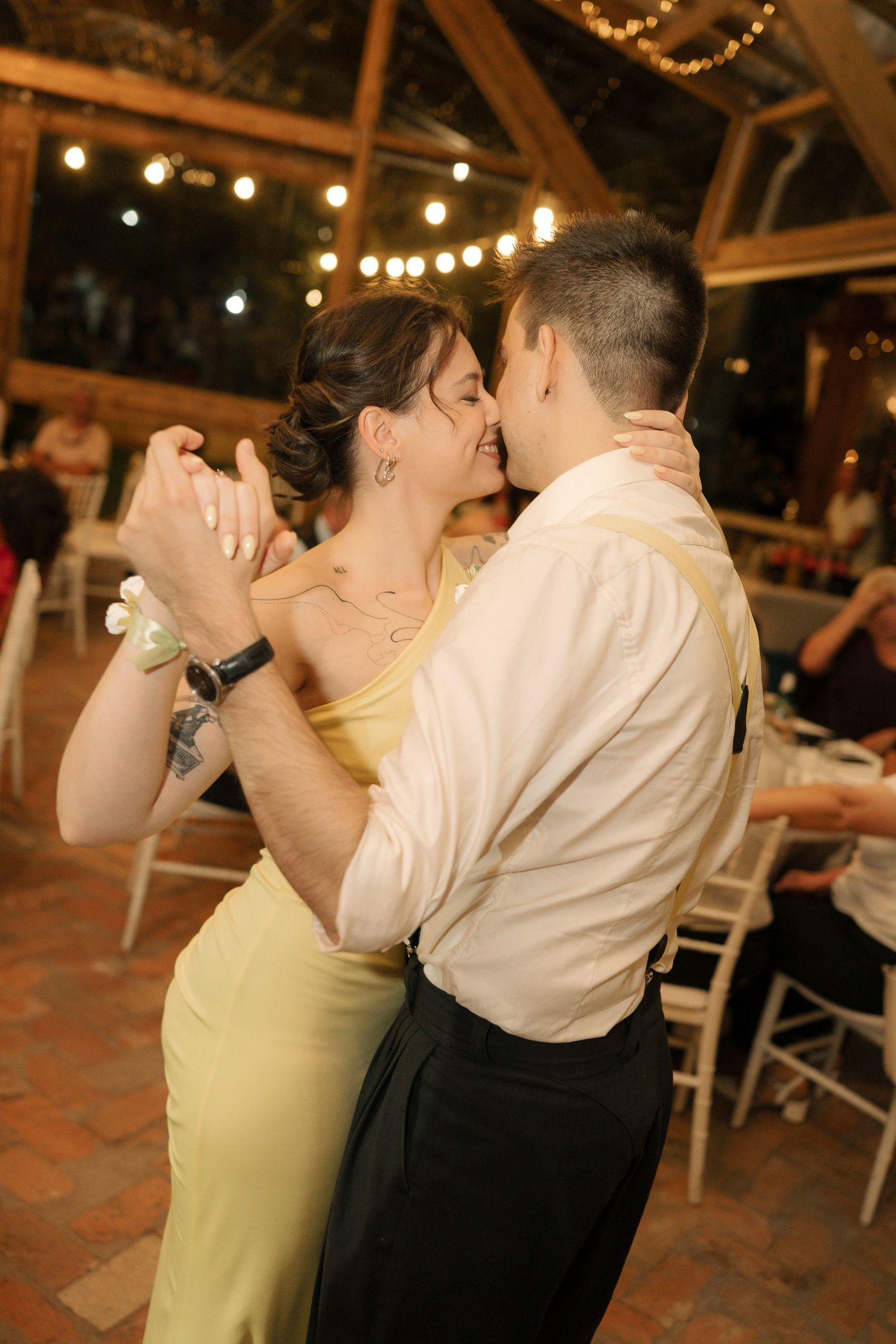 A couple shares a romantic dance moment under twinkling lights at an evening wedding reception.