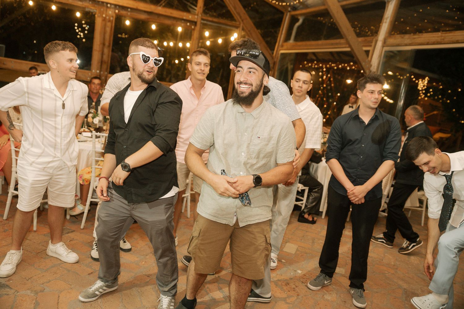 A group of people dancing and having fun at a festive outdoor venue with string lights overhead.