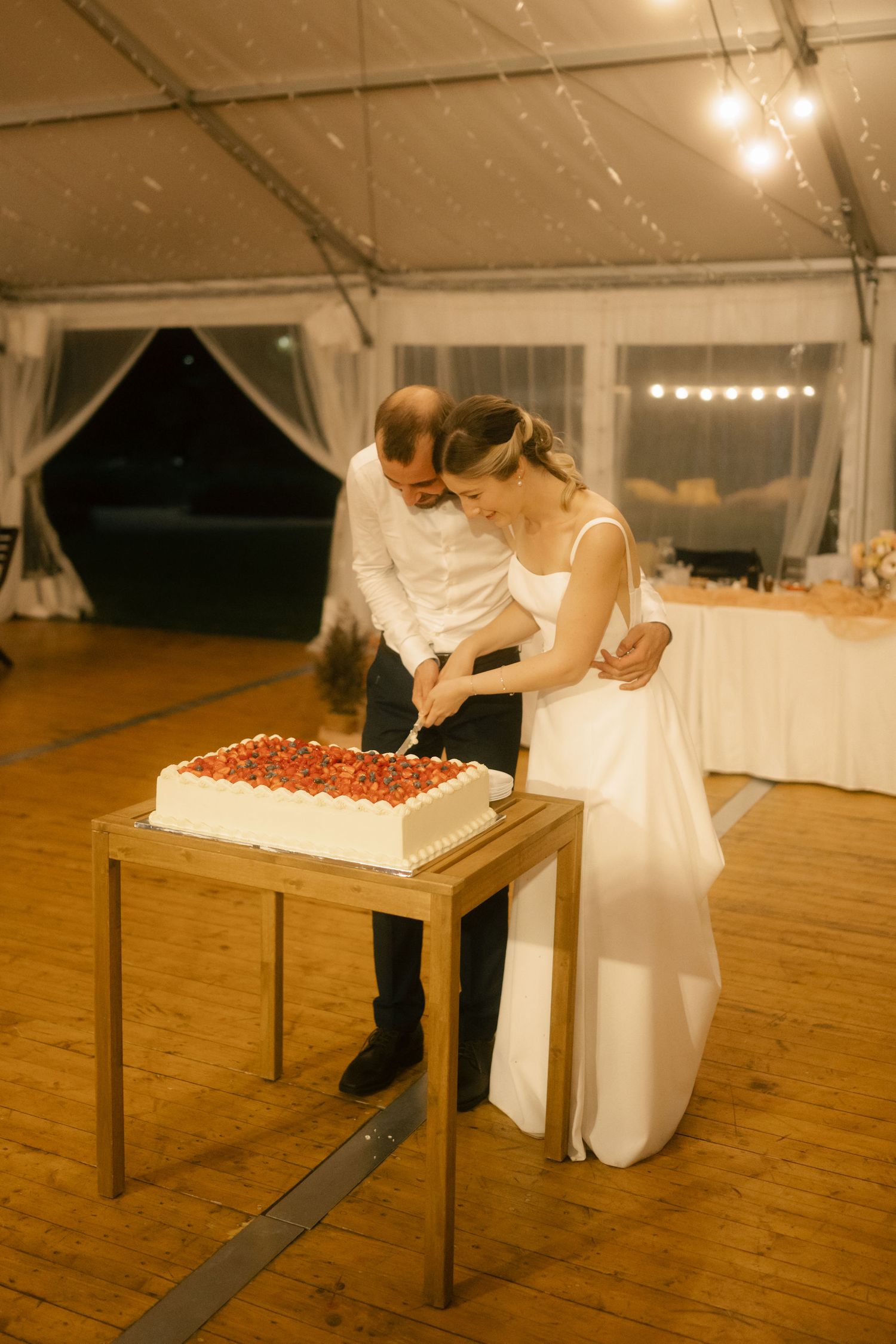 Couple in wedding attire shares a romantic moment at reception while leaning over a table in a white tent venue.