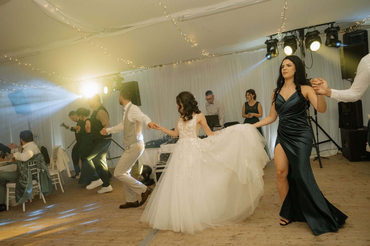 Bride in white gown dancing with guests in elegant wedding reception venue with festive lighting.
