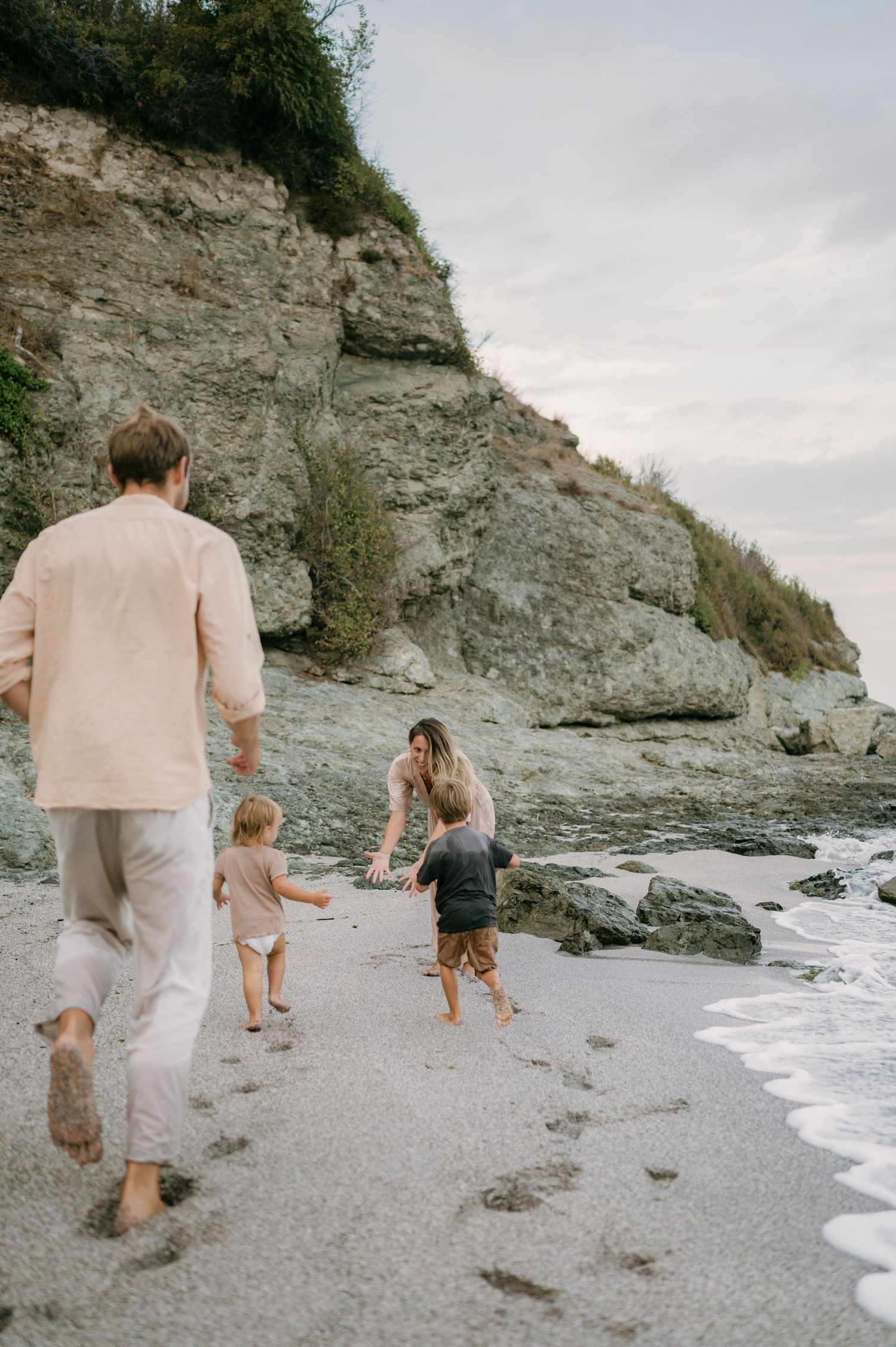 Family walking barefoot on a rocky beach shoreline, with two young children and parents enjoying a seaside outing.