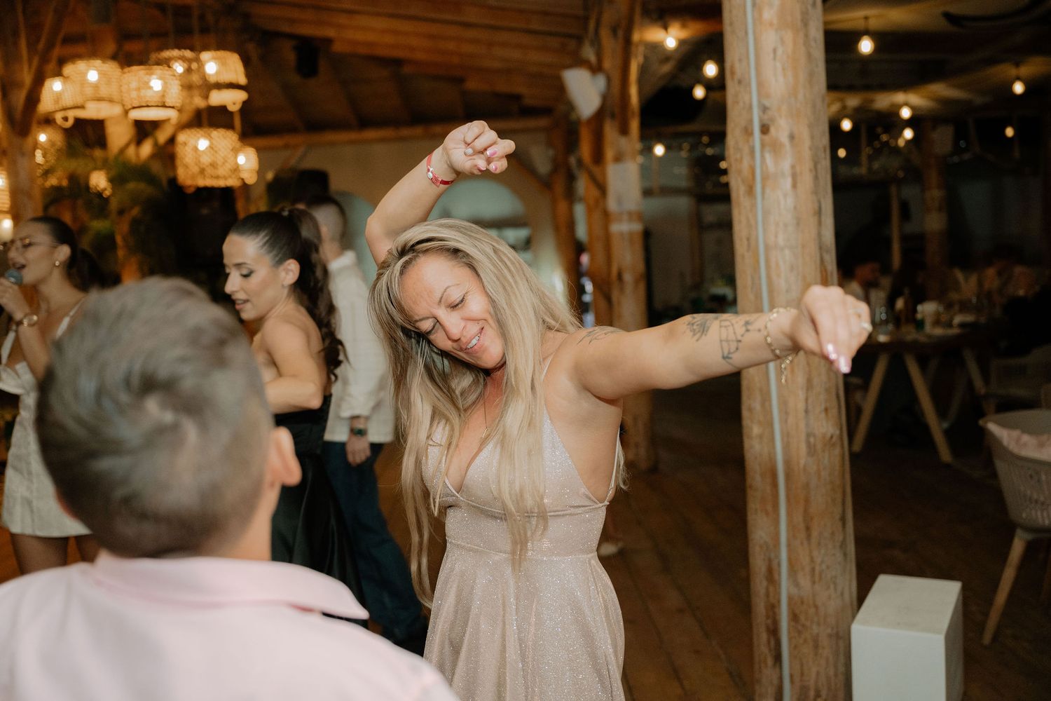 Wedding guests dance and celebrate on a rustic wooden dance floor under warm lighting at a barn reception venue.