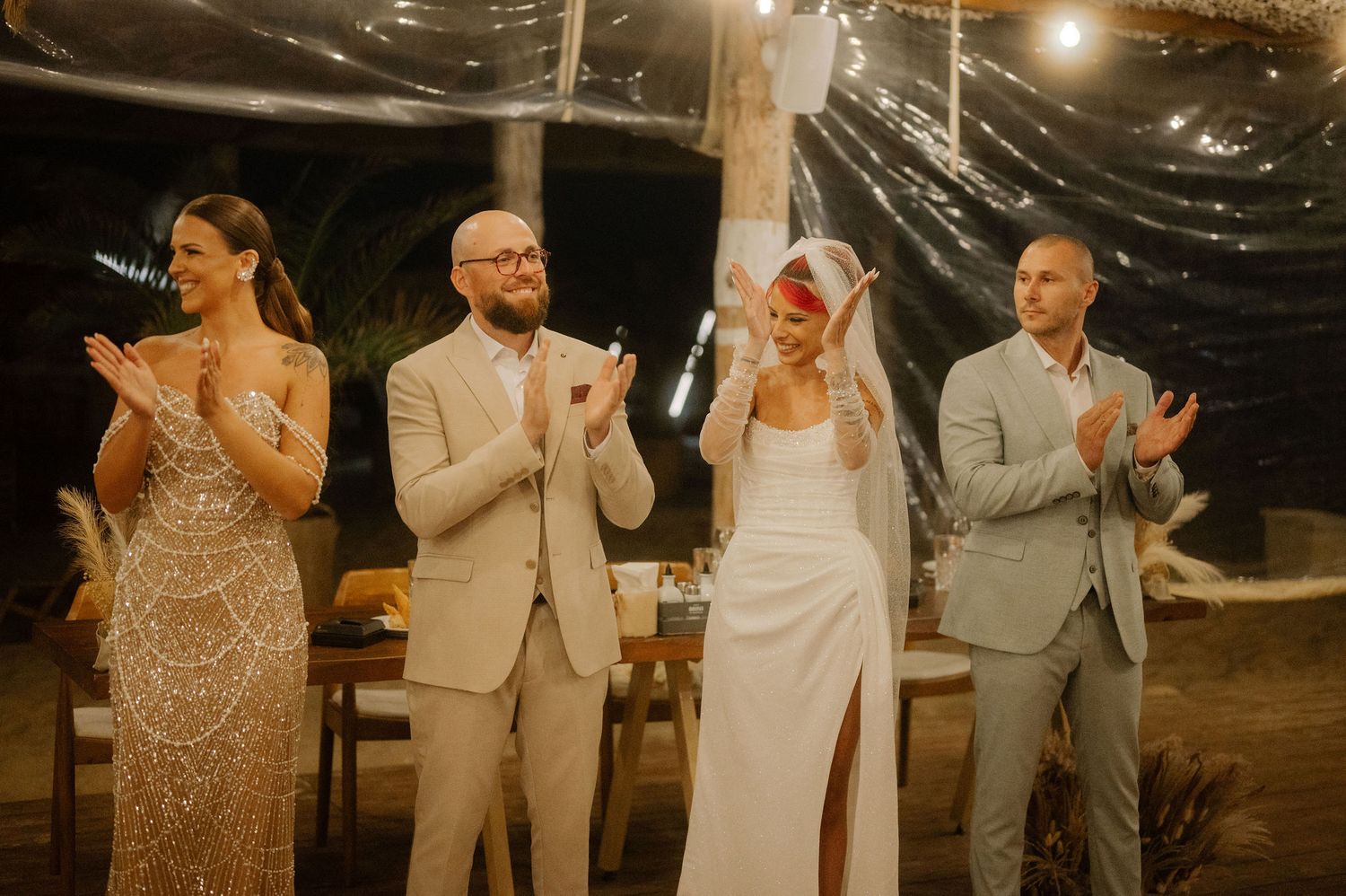 Wedding party stands together clapping during an evening outdoor celebration.