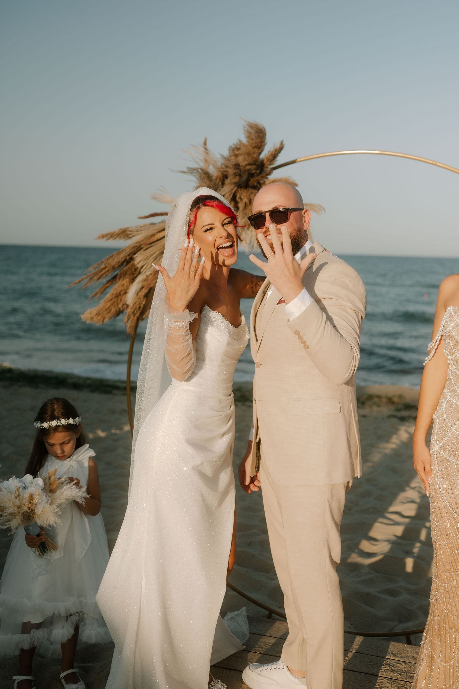 A couple dances joyfully together on a beach at sunset with their hair blowing in the wind.