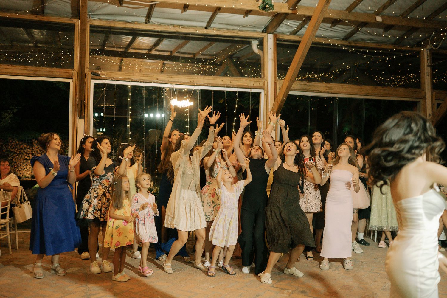 Wedding guests dance with raised arms on a rustic barn dance floor during an evening reception celebration.