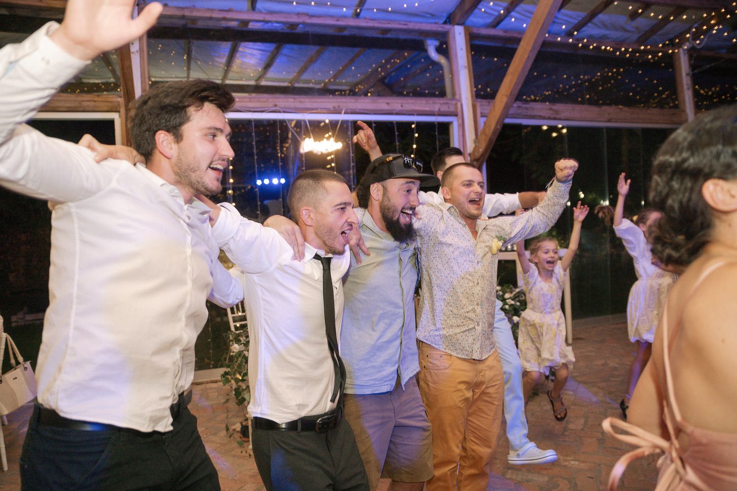 Wedding guests dancing and celebrating together under purple lighting at a reception party.