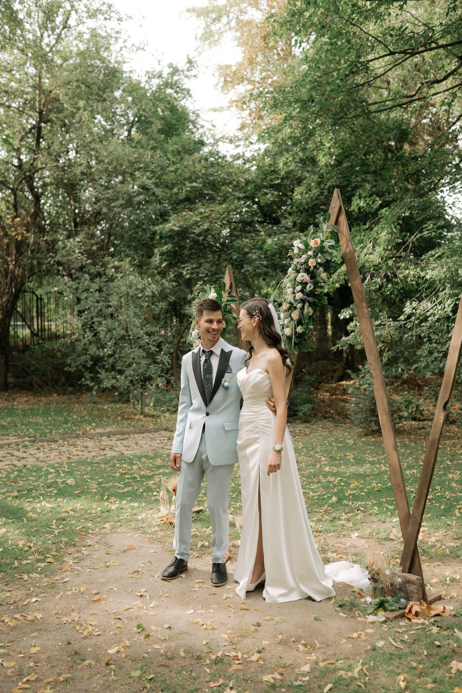 A couple shares intimate moments in an outdoor garden setting wearing elegant wedding attire.