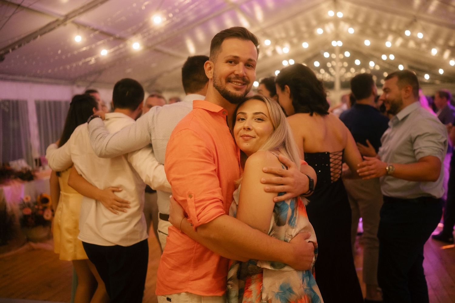 Wedding guests dancing and celebrating on a wooden dance floor under twinkling lights.