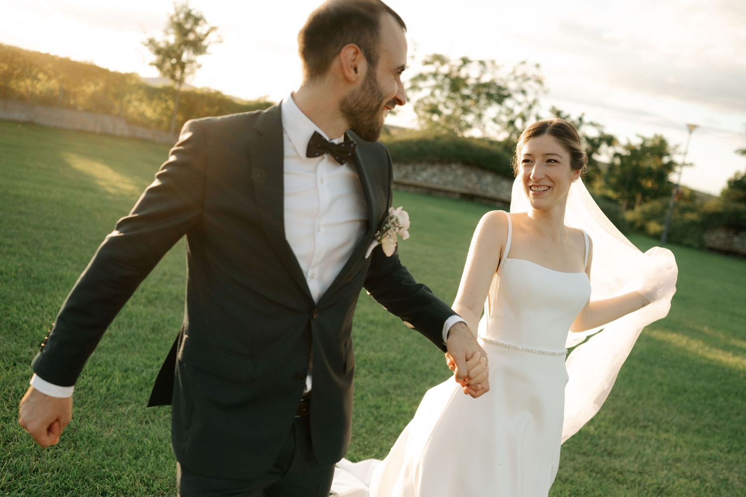 Bride and groom share a romantic dance together on a sunlit grassy lawn during their wedding celebration.