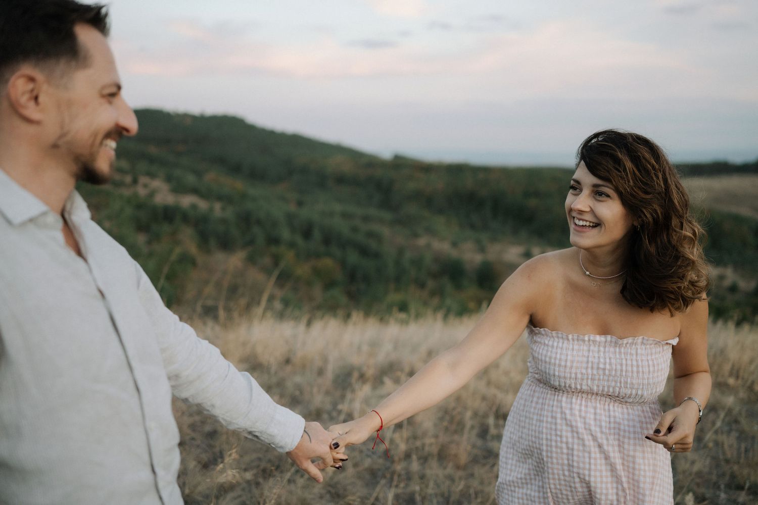 A couple shares intimate moments in a scenic outdoor setting with rolling hills and natural light.