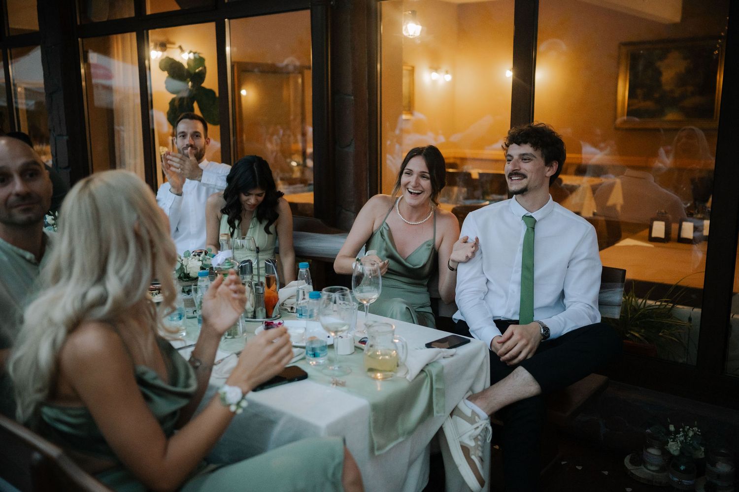 Wedding guests enjoying dinner and conversation at elegantly decorated reception tables in warm candlelit setting.