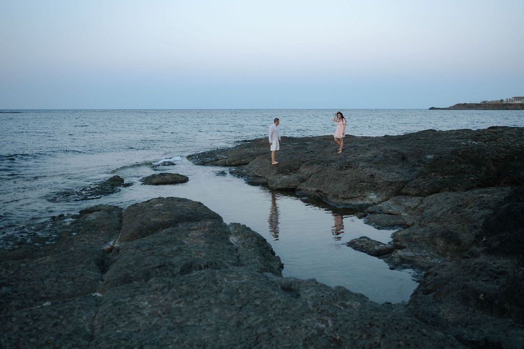 Rocky coastline with tide pools and ocean waves stretching along a beach at dusk.
