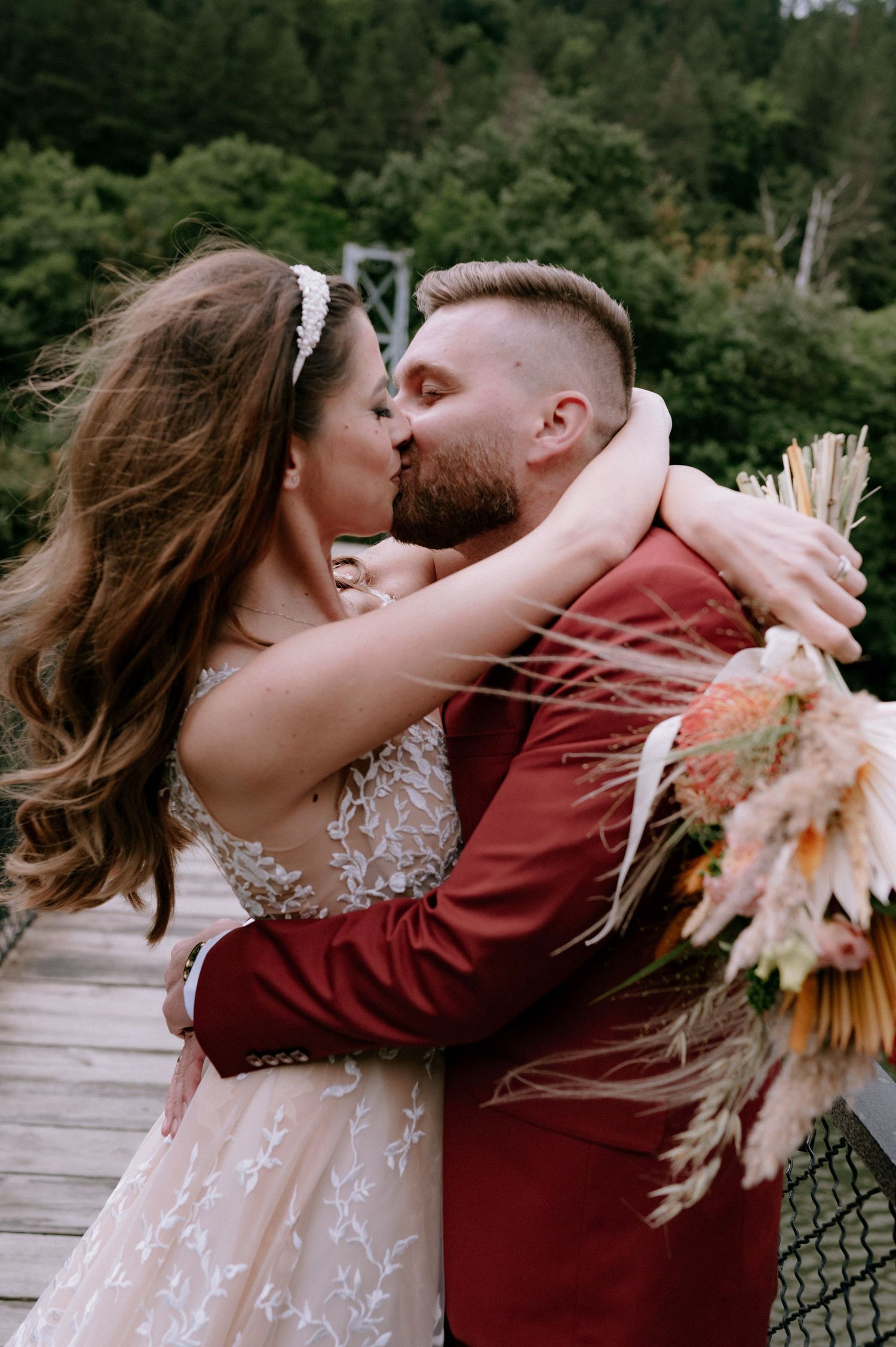 A romantic couple shares a tender kiss while holding a dried floral bouquet in warm autumn tones.