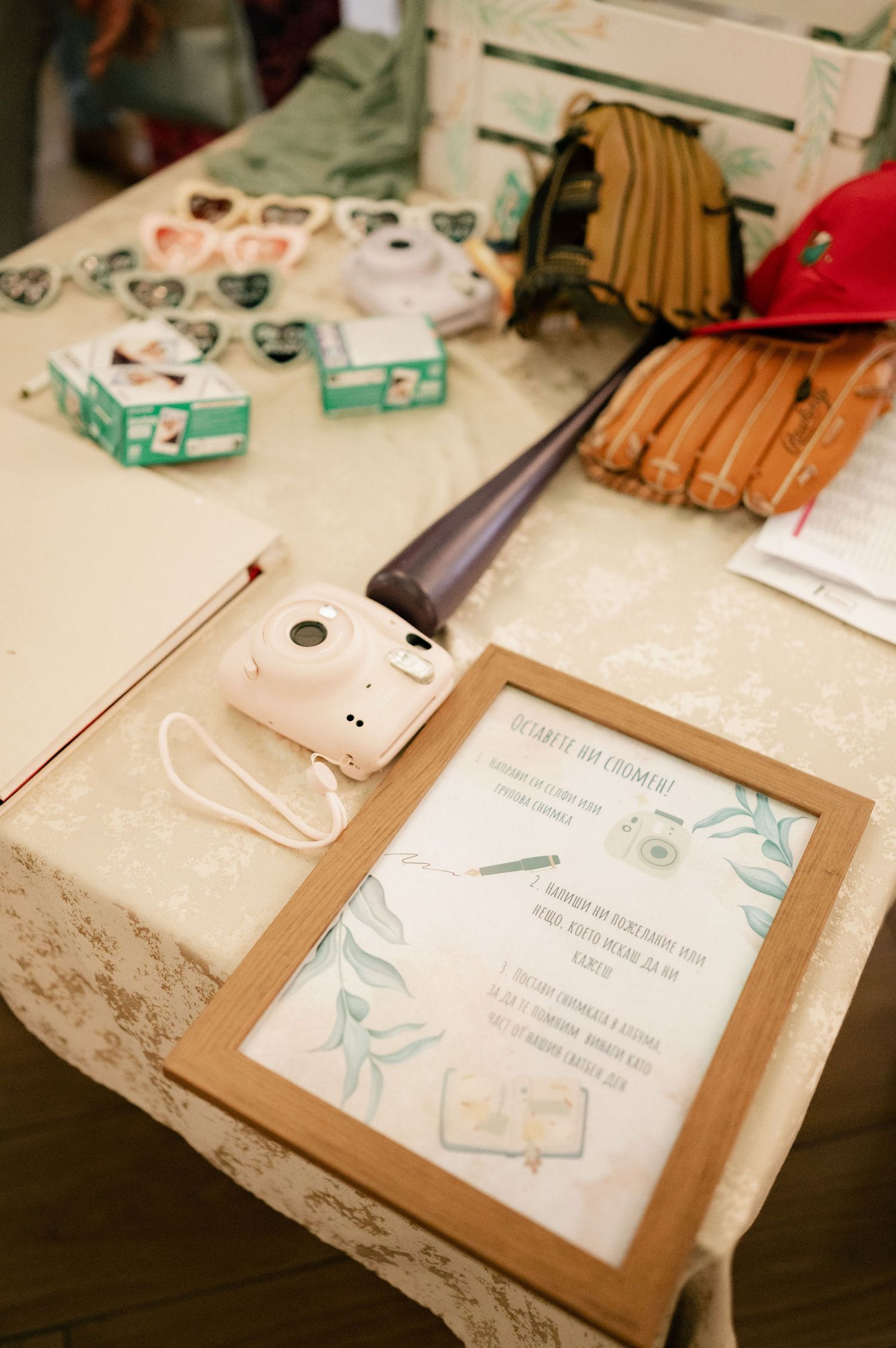 A vintage camera and framed invitation sit on a lace tablecloth next to baseball gloves and playing cards.