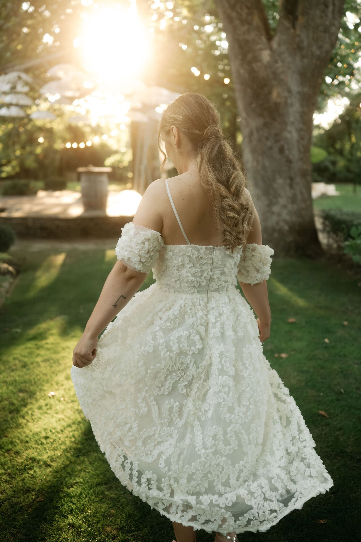 A bride in a flowing white lace dress twirls in a garden at sunset, creating a dreamy silhouette against golden light.