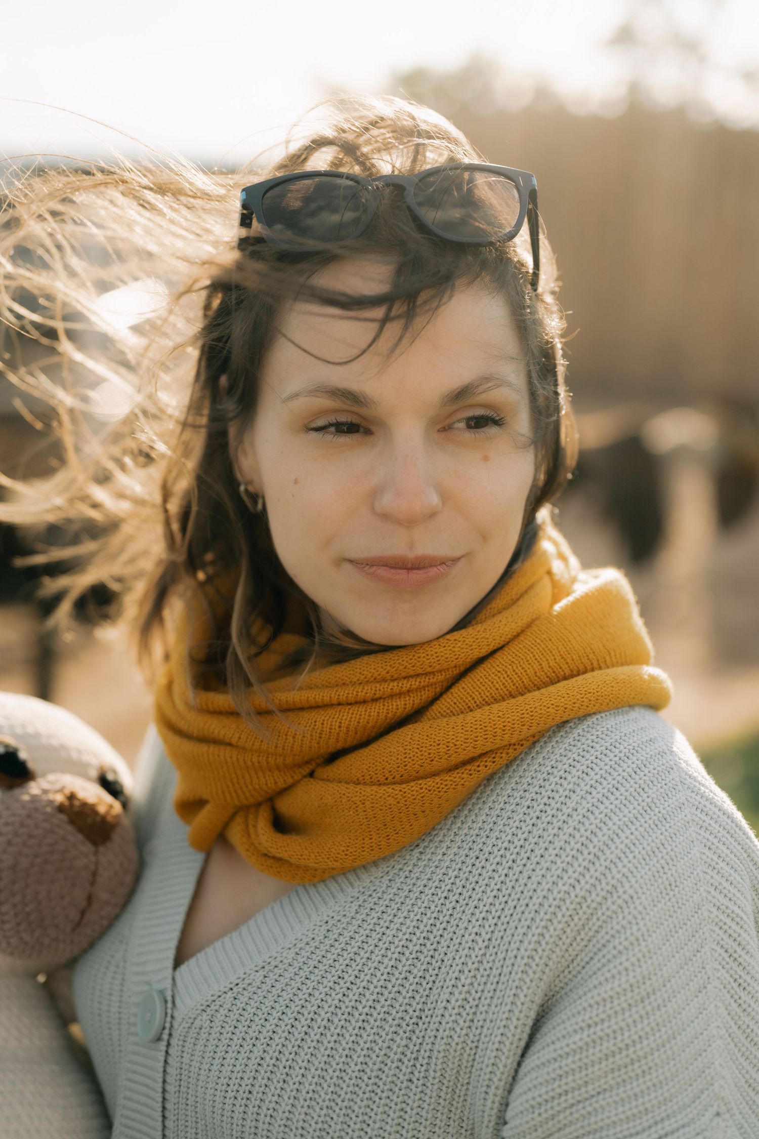Person wearing a cozy yellow scarf and light gray sweater smiles warmly on a bright autumn day.