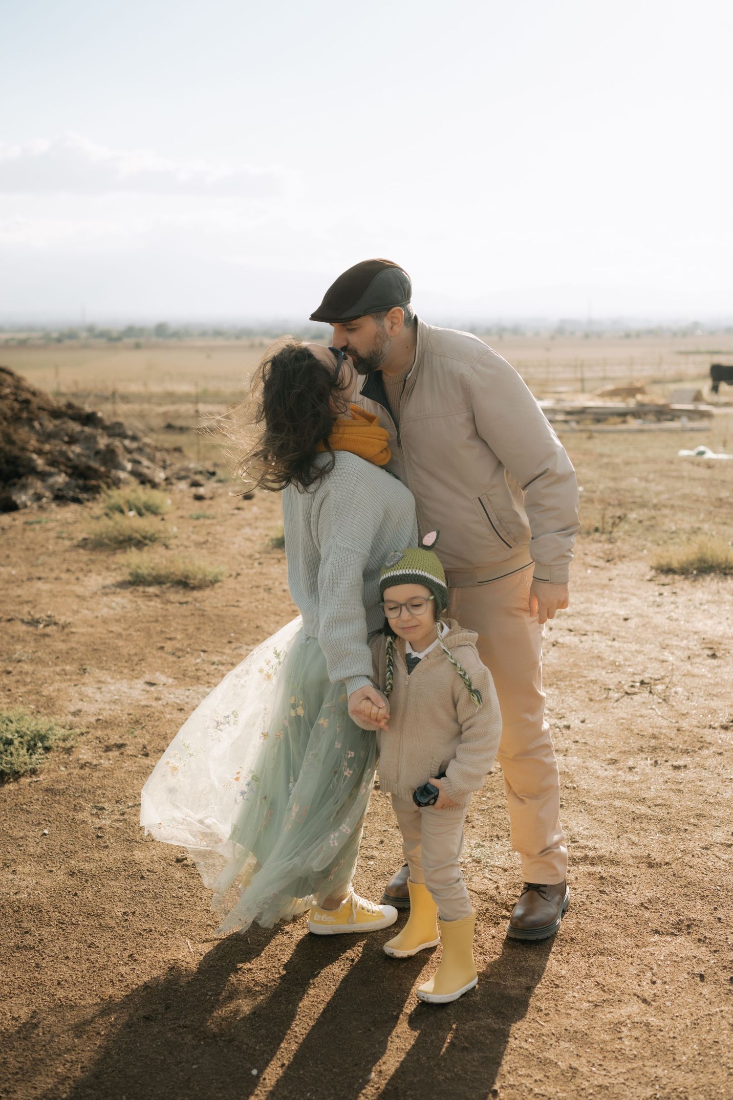 A couple shares a tender moment on a dusty hillside path in matching beige and mint colored outfits.