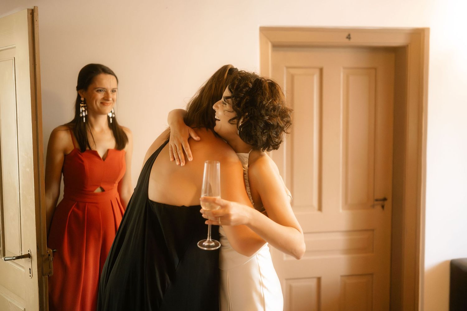A group of people in formal attire gather in an elegant room with warm lighting and wooden doors.